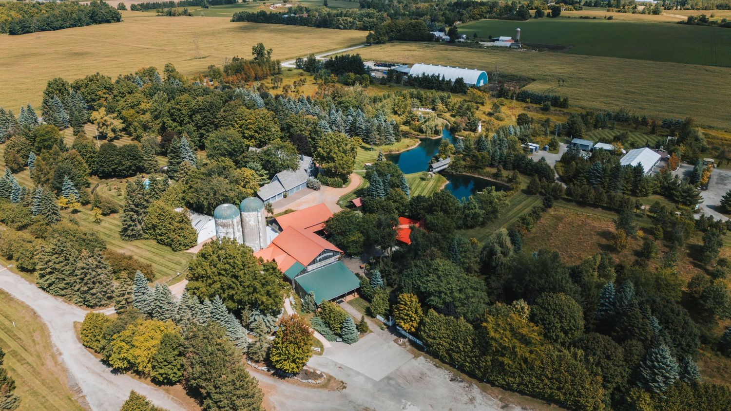 Aerial panoramic view of rural farmland with scattered buildings and dense tree lines stretching across rolling hills.