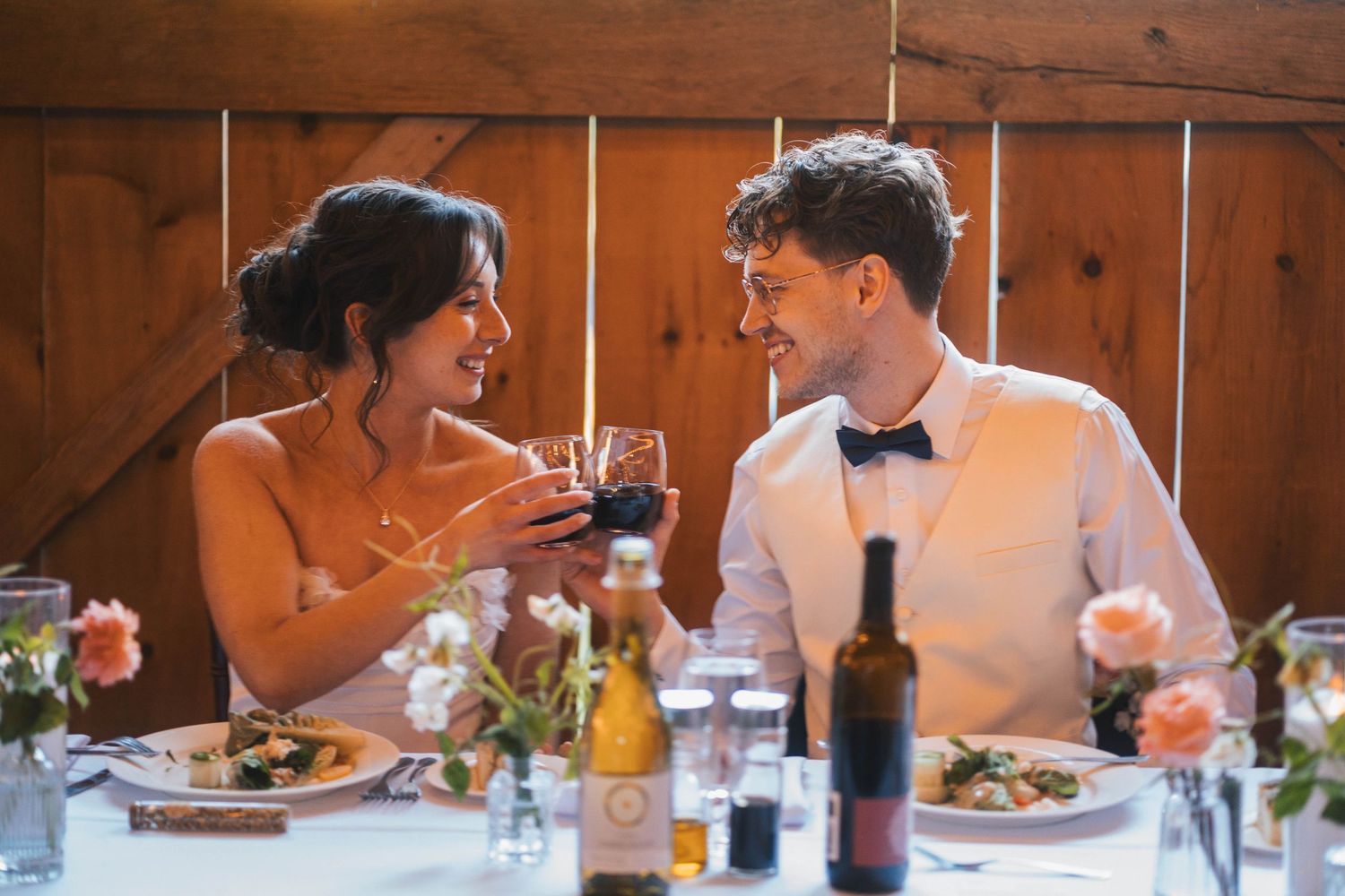 Wedding guests enjoying a meal together at a rustic wooden table during an elegant reception dinner service.
