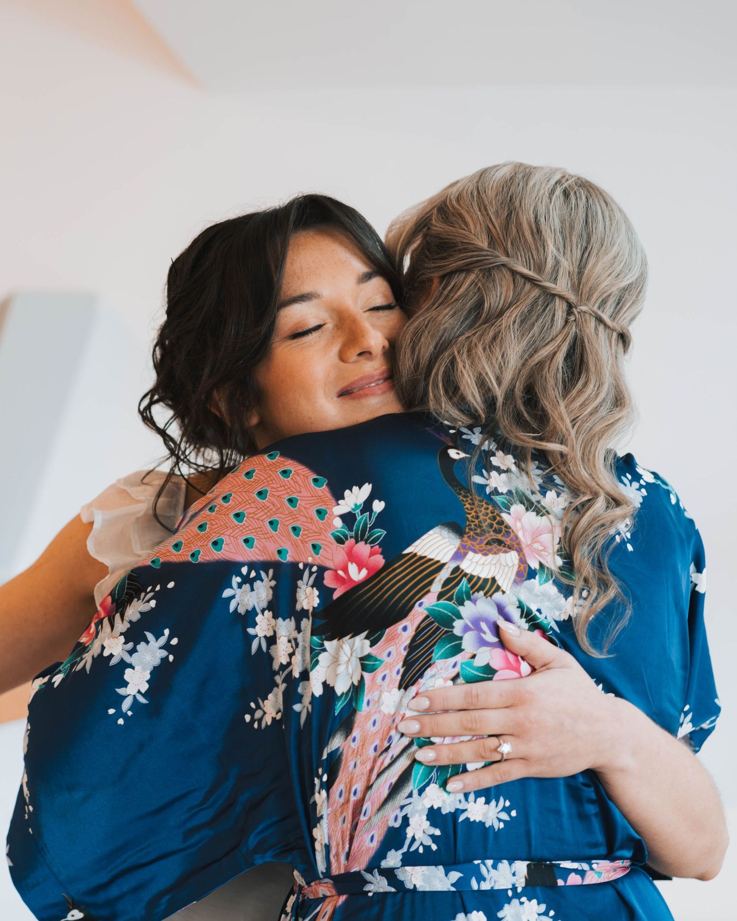 Two people share an emotional embrace while wearing a blue floral dress and pink floral outfit.