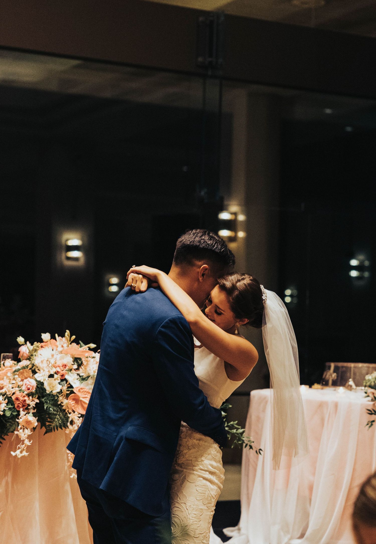 A romantic first dance moment at a wedding reception with floral decorations and ambient lighting in the background.
