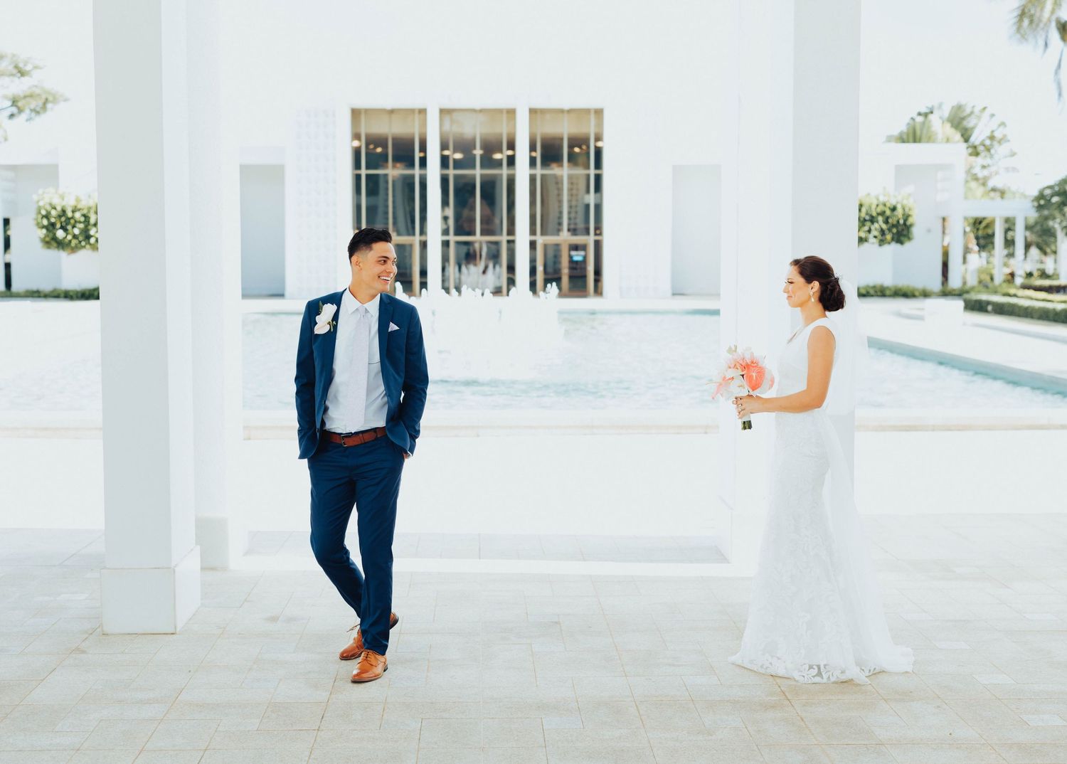 A couple in wedding attire walks together on a bright white columned porch during their special day.