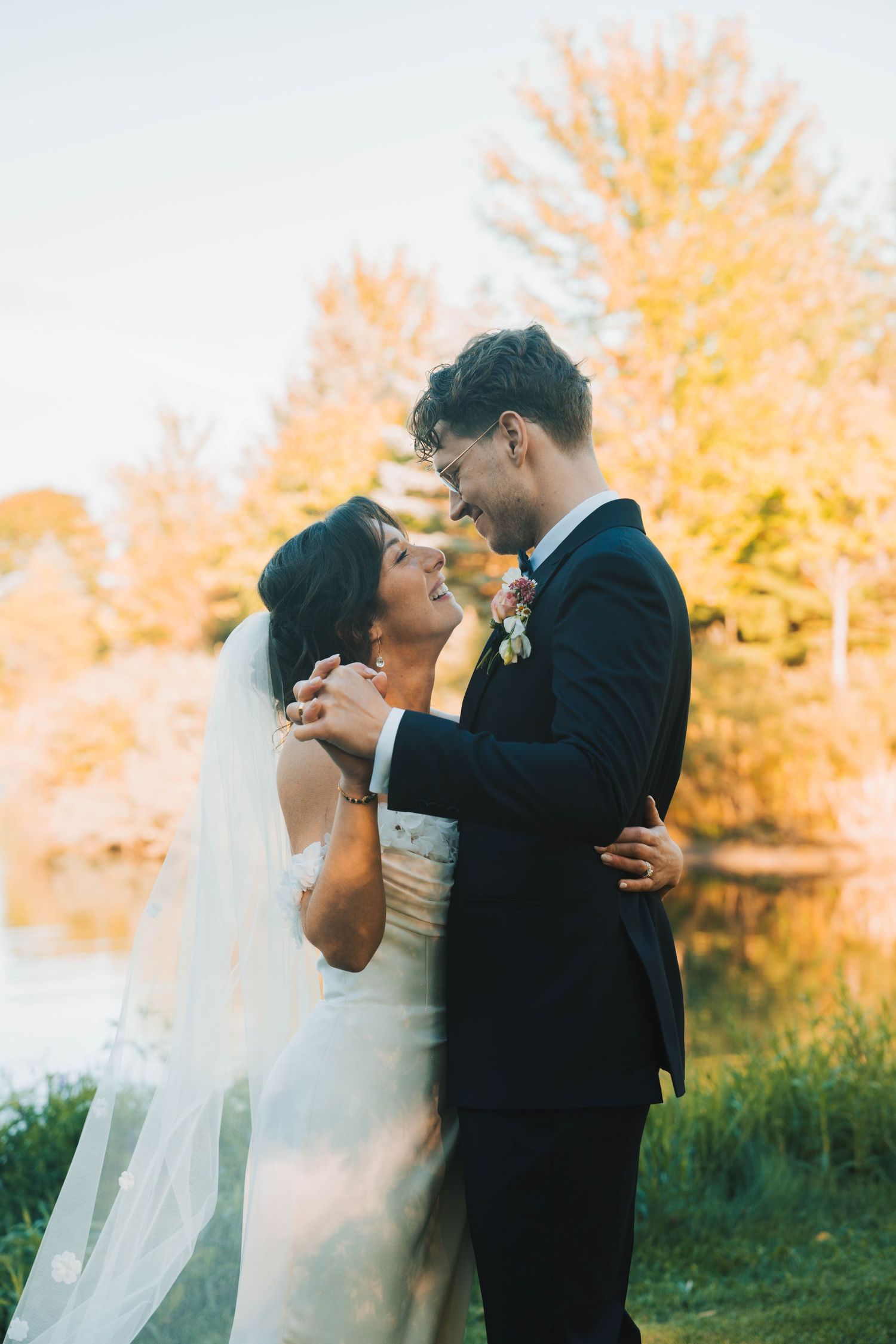 Romantic wedding couple embraces in autumn sunlight with golden foliage in background.