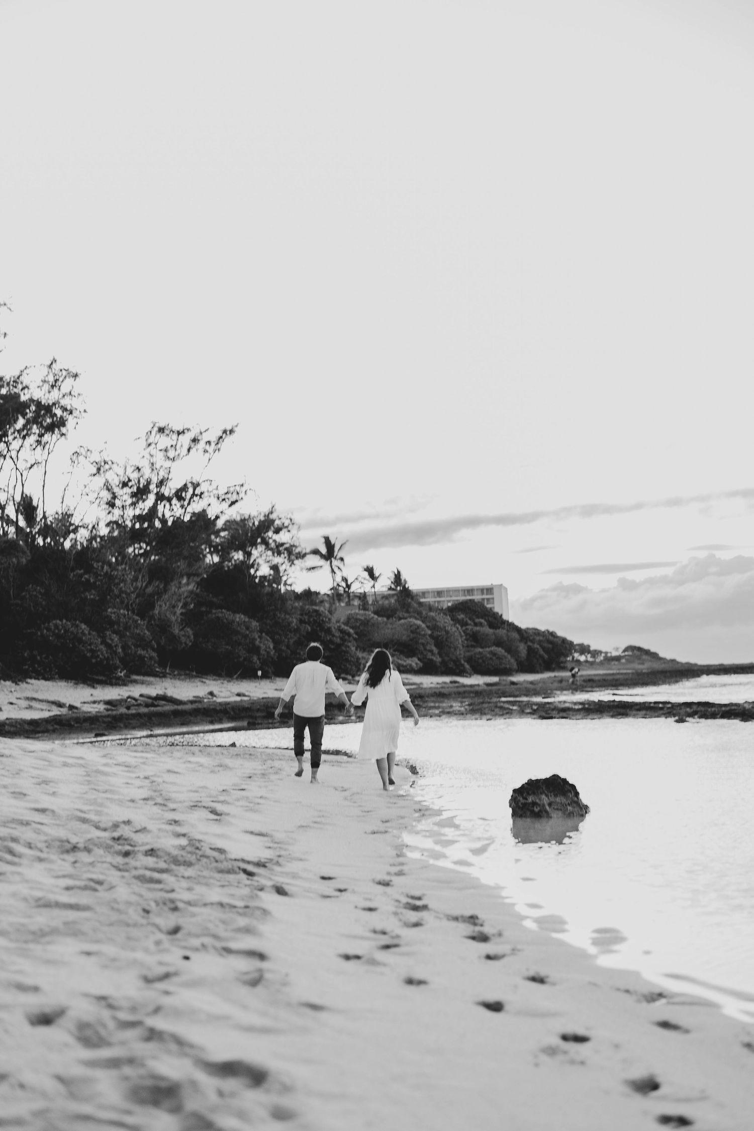 Black and white photograph of a couple walking along a serene beach shoreline.