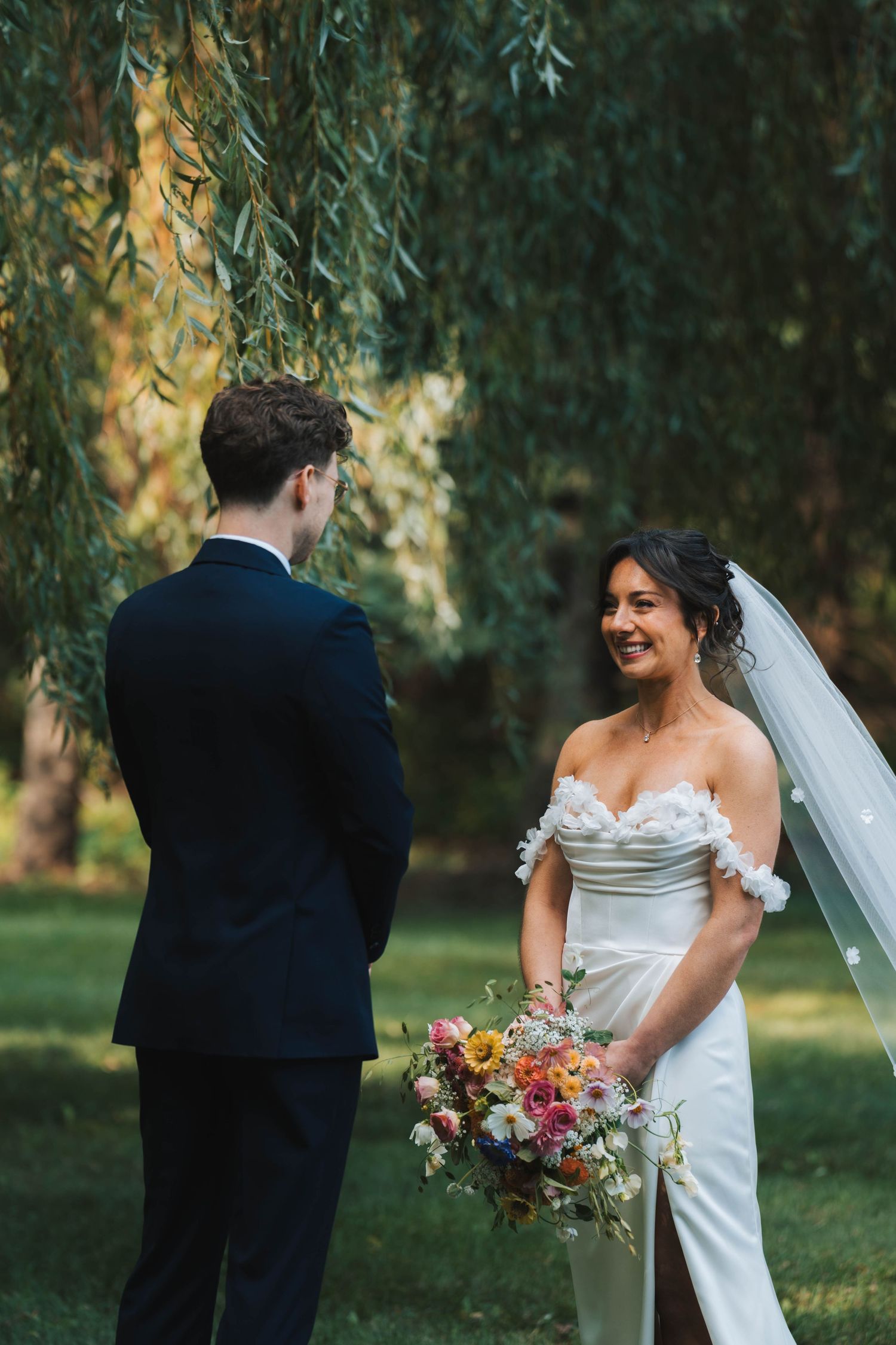 Wedding couple shares first look moment under weeping willow trees.