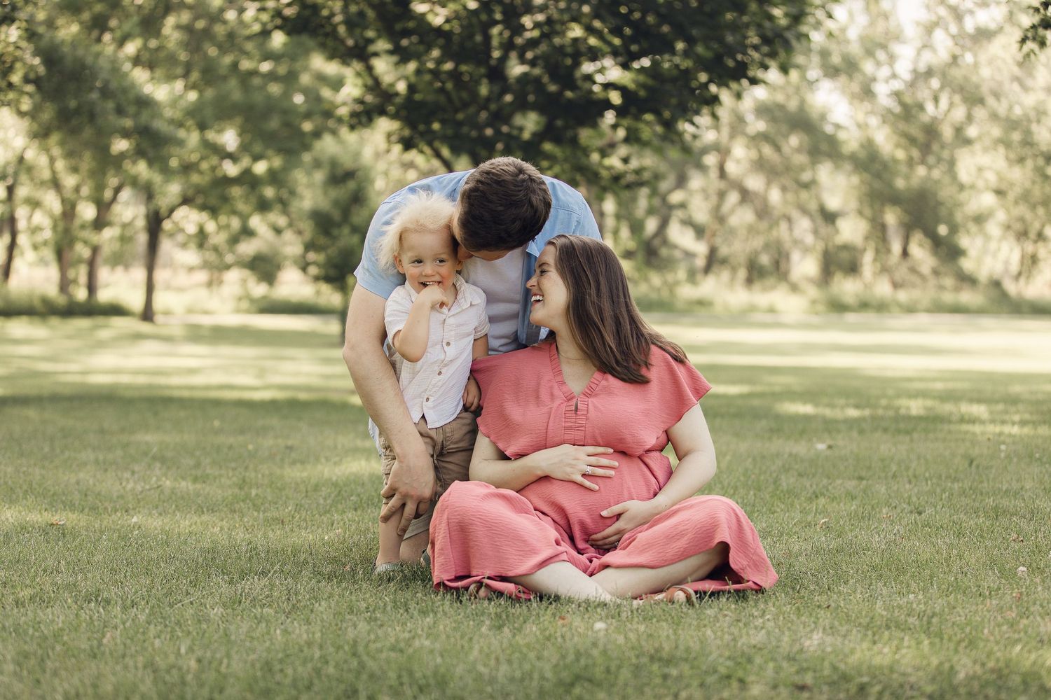 A family relaxes together on grass in a park during maternity photo session.