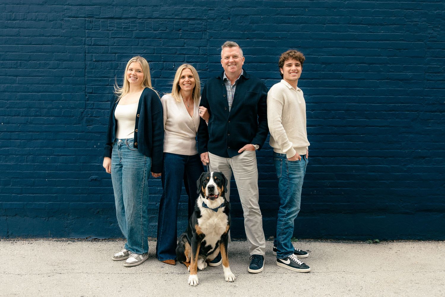 Family portrait with a black and white dog against a dark blue brick wall.