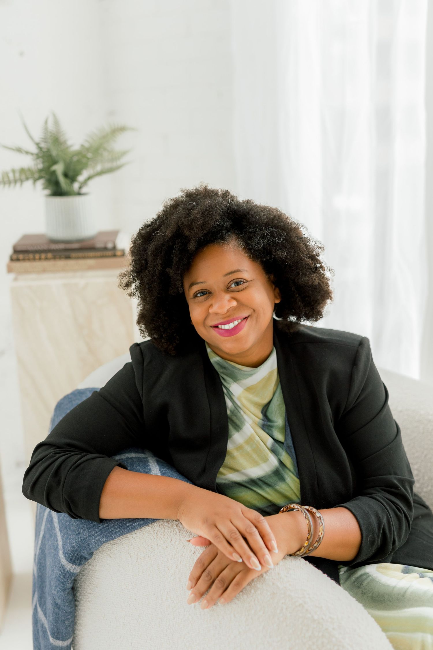 Professional in black blazer and green top poses on light colored furniture.