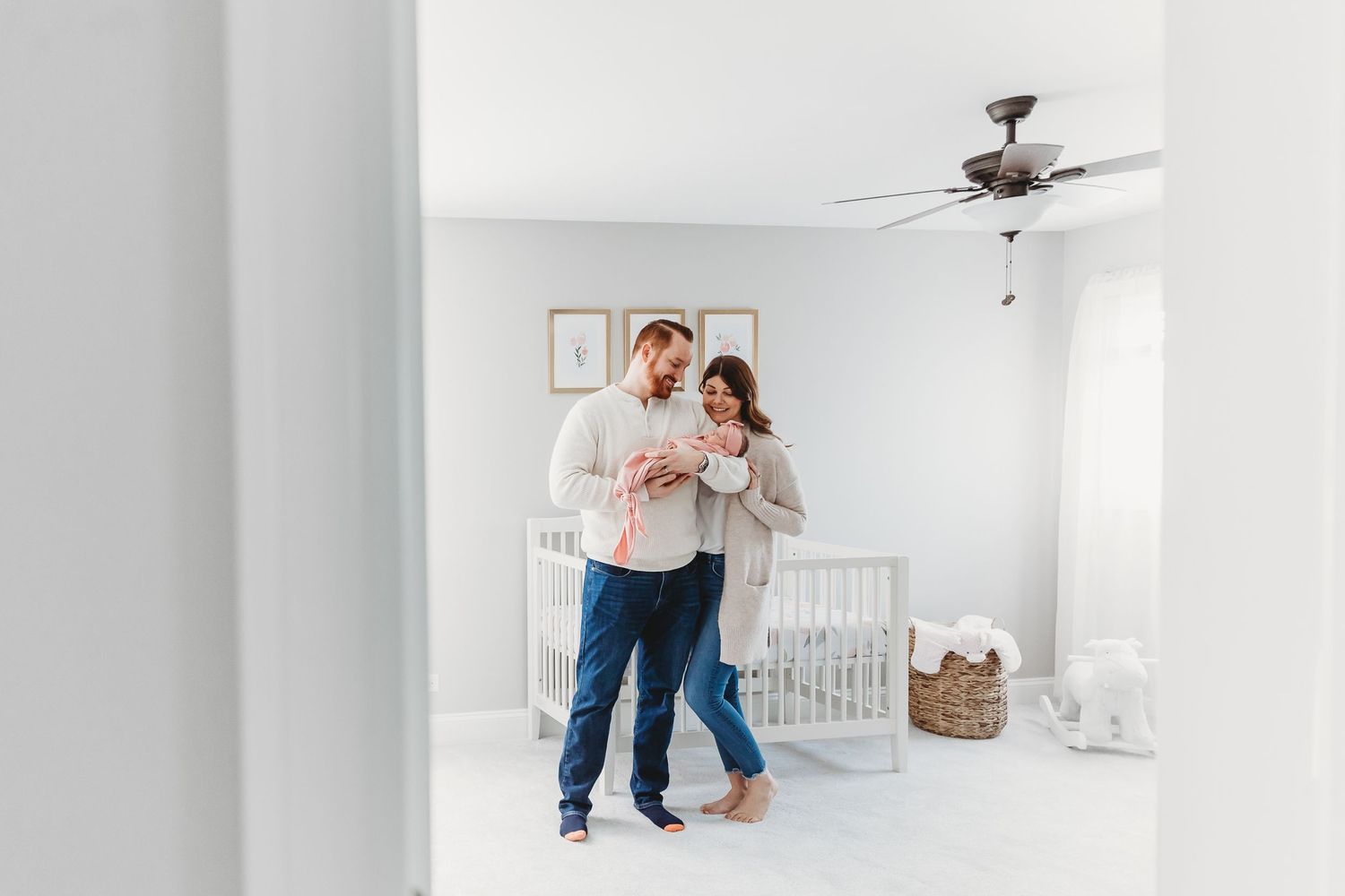 A couple stands together in a bright white nursery room with a crib.