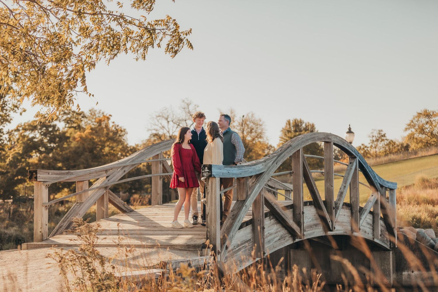 A rustic wooden footbridge in an autumn landscape during golden hour with fall foliage in the background.