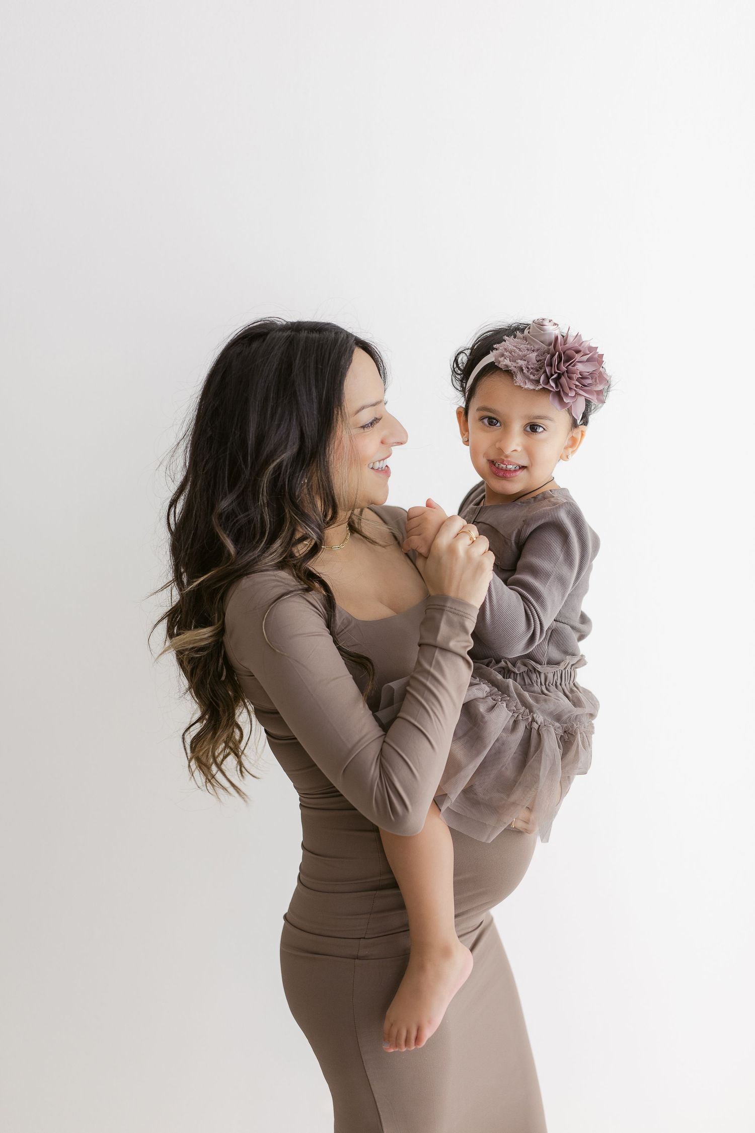 Mother and child wearing matching mauve outfits pose together against white background.