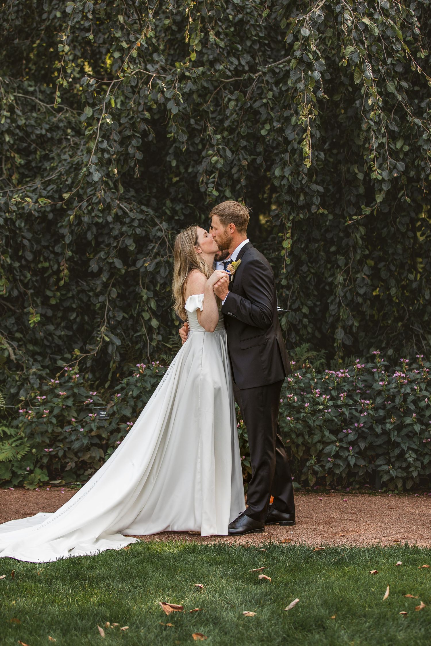 A romantic wedding couple shares intimate kisses in a garden setting with a flowing white dress and lush greenery background.