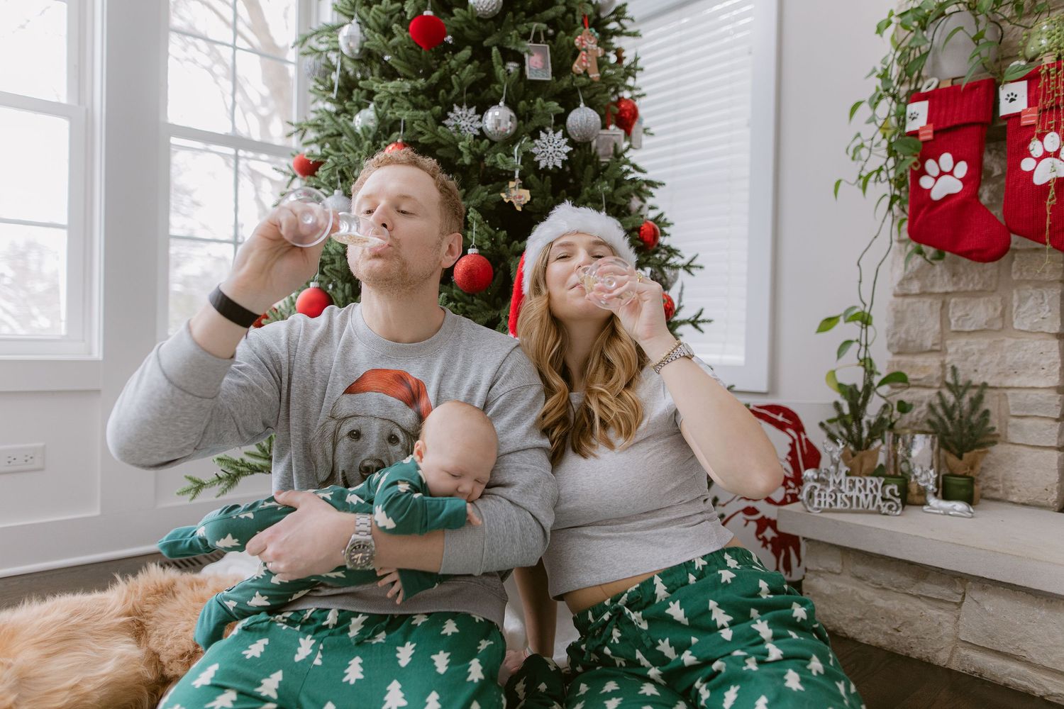 Family in festive green outfits posing by Christmas tree with golden retriever.