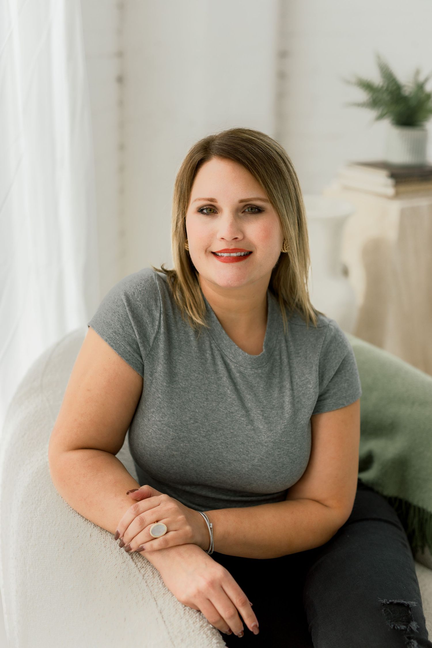 Professional headshot wearing gray t-shirt seated on white couch.