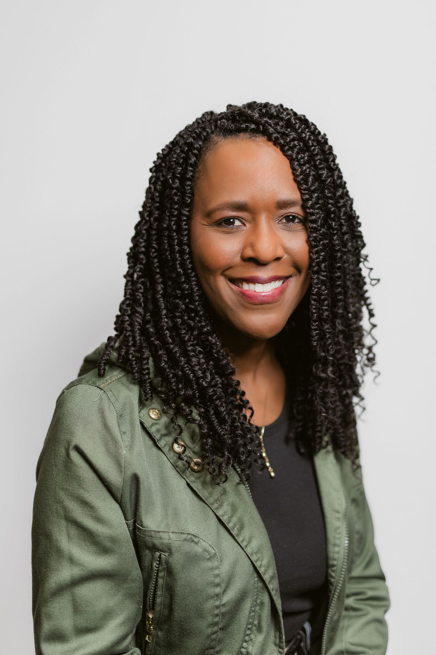 Professional portraits of person in olive jacket with curly hair against light background.