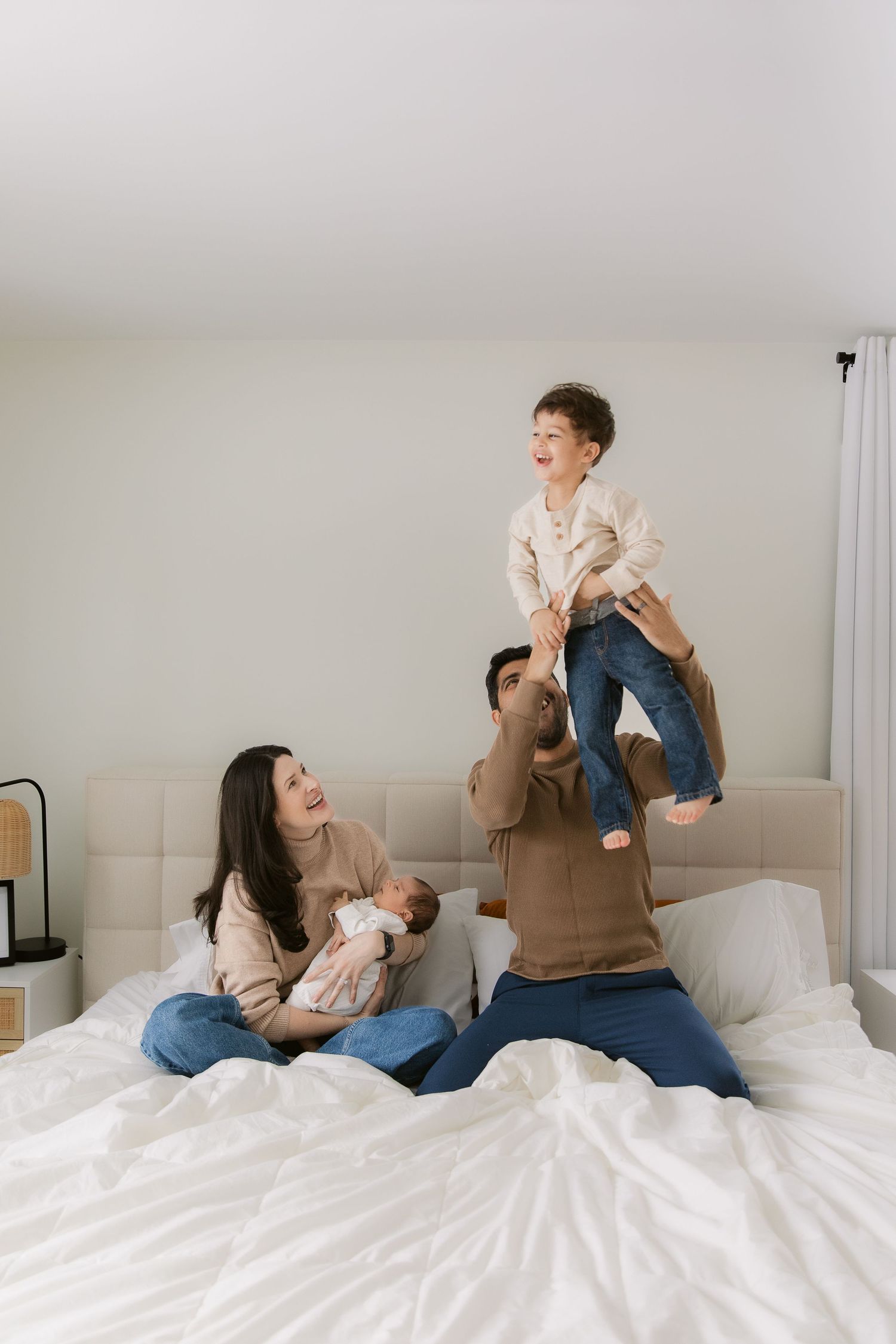 A playful sequence showing a parent and child having fun together on a white bed in a bright minimalist room.