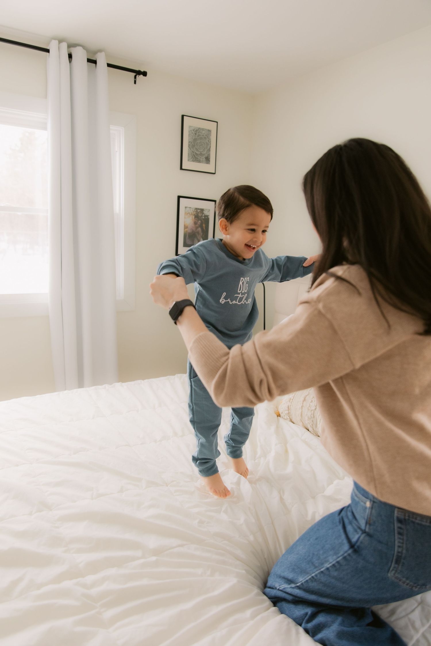 A playful moment captured on a white bed as a child in blue pajamas jumps while being supported.