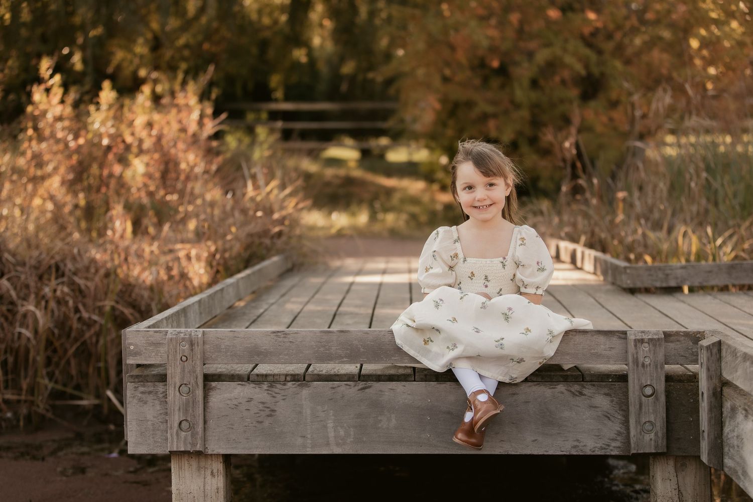 Child exploring wooden boardwalk during autumn sunset photo session.