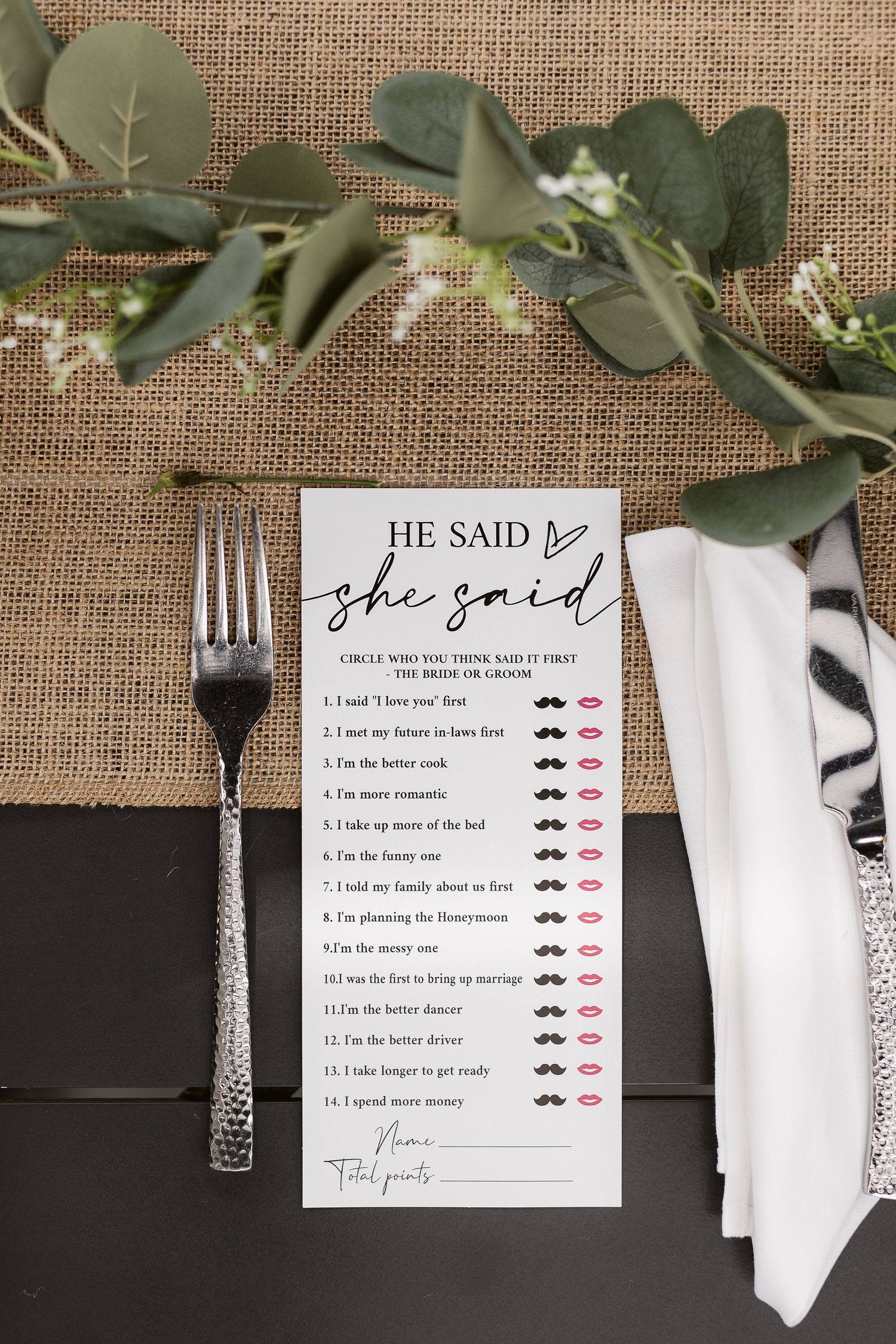 He Said She Said bridal shower game card on a rustic burlap table setting with greenery, fork, and napkin.