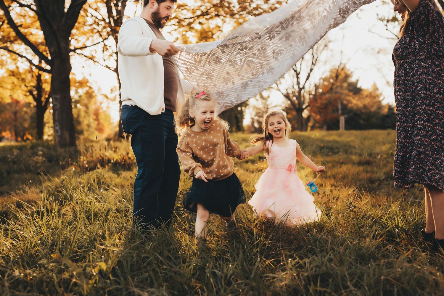 A family enjoys a playful moment together in a golden sunlit field during sunset.