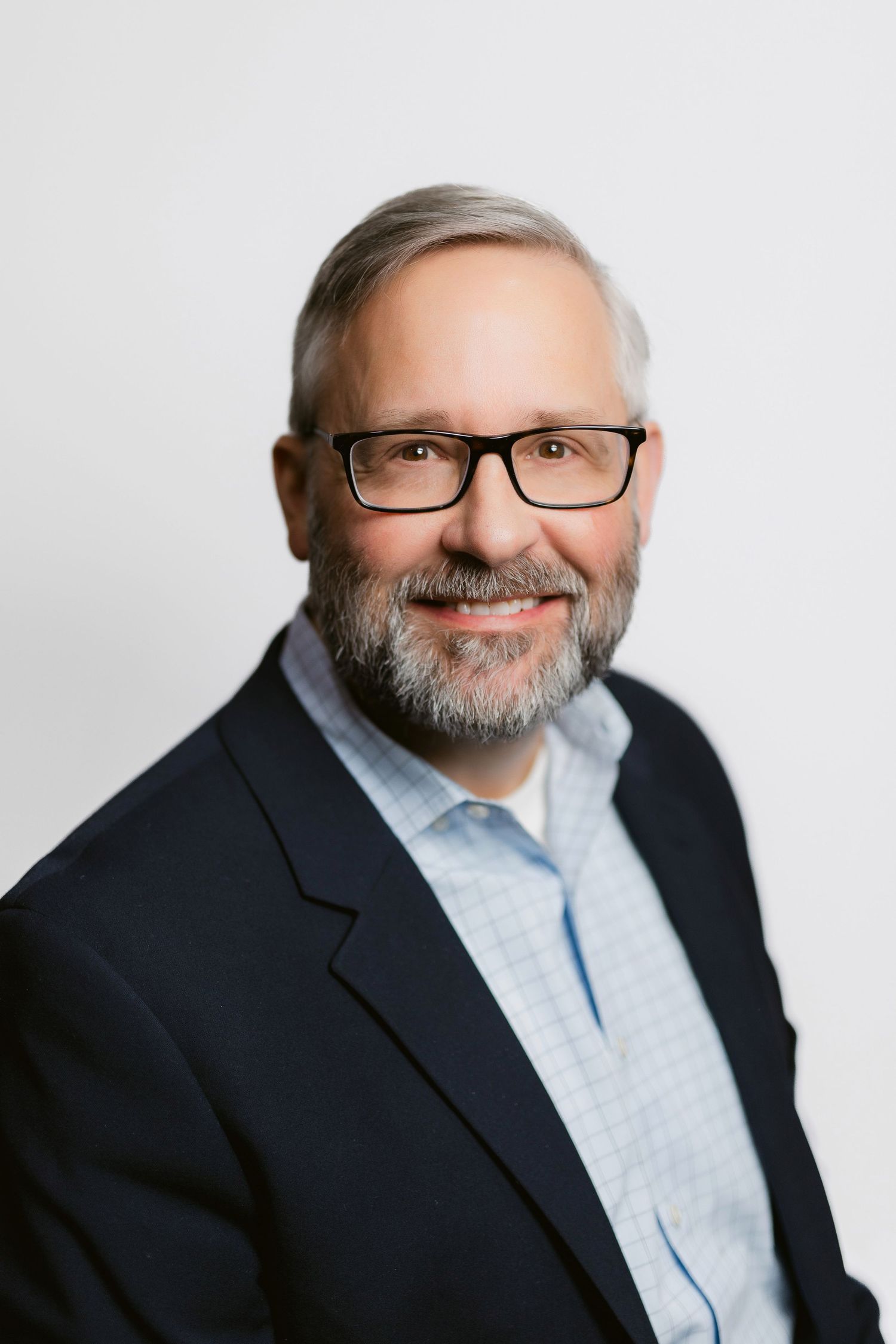 Professional portraits of a person with glasses wearing navy blazer against white background.