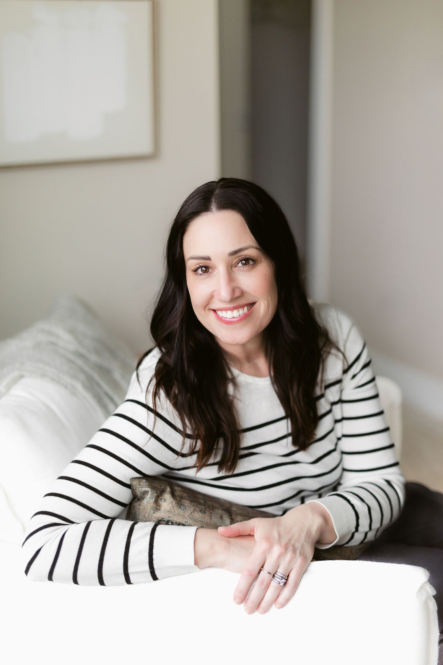 Casual portrait series in striped sweater against white bedding and neutral wall.
