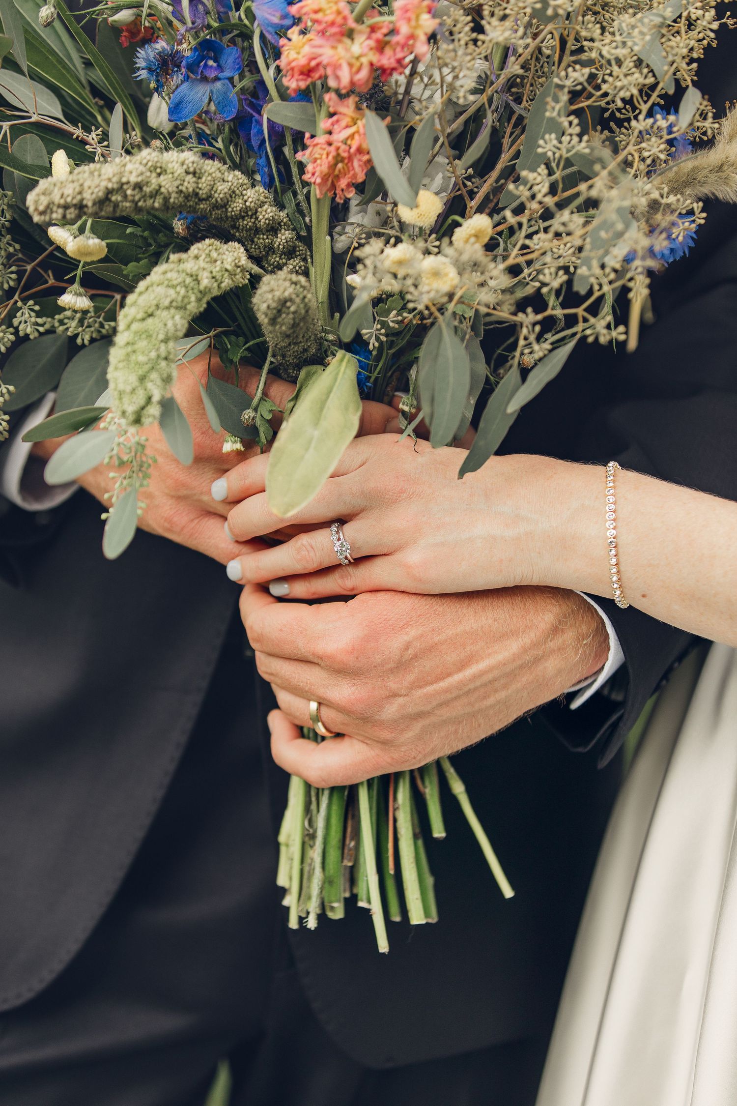 Close-up view of hands holding a delicate bouquet with coral flowers and white baby's breath against a dark background.