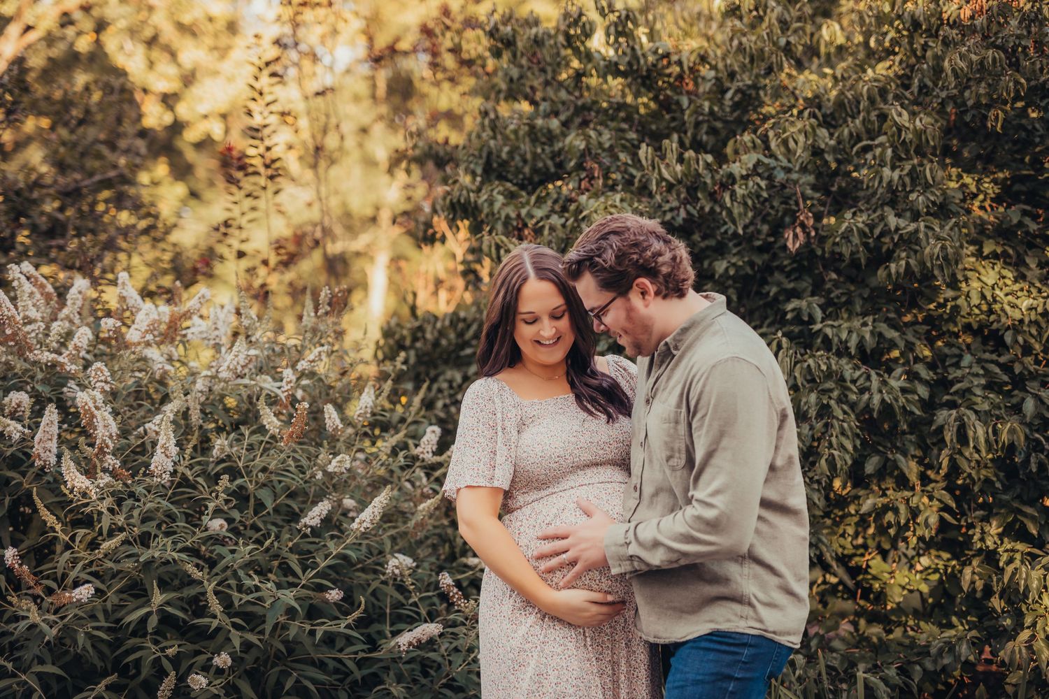 Couple embraces outdoors in nature setting during autumn maternity photo session.