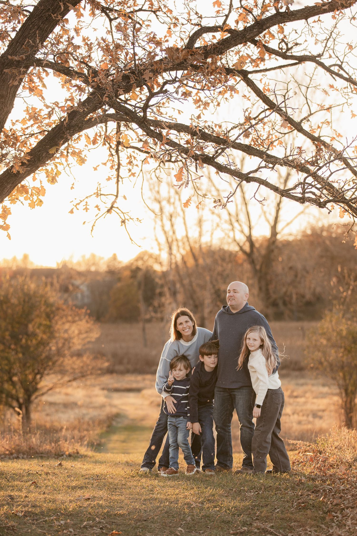 Family gathering under autumn trees during golden hour photography session.