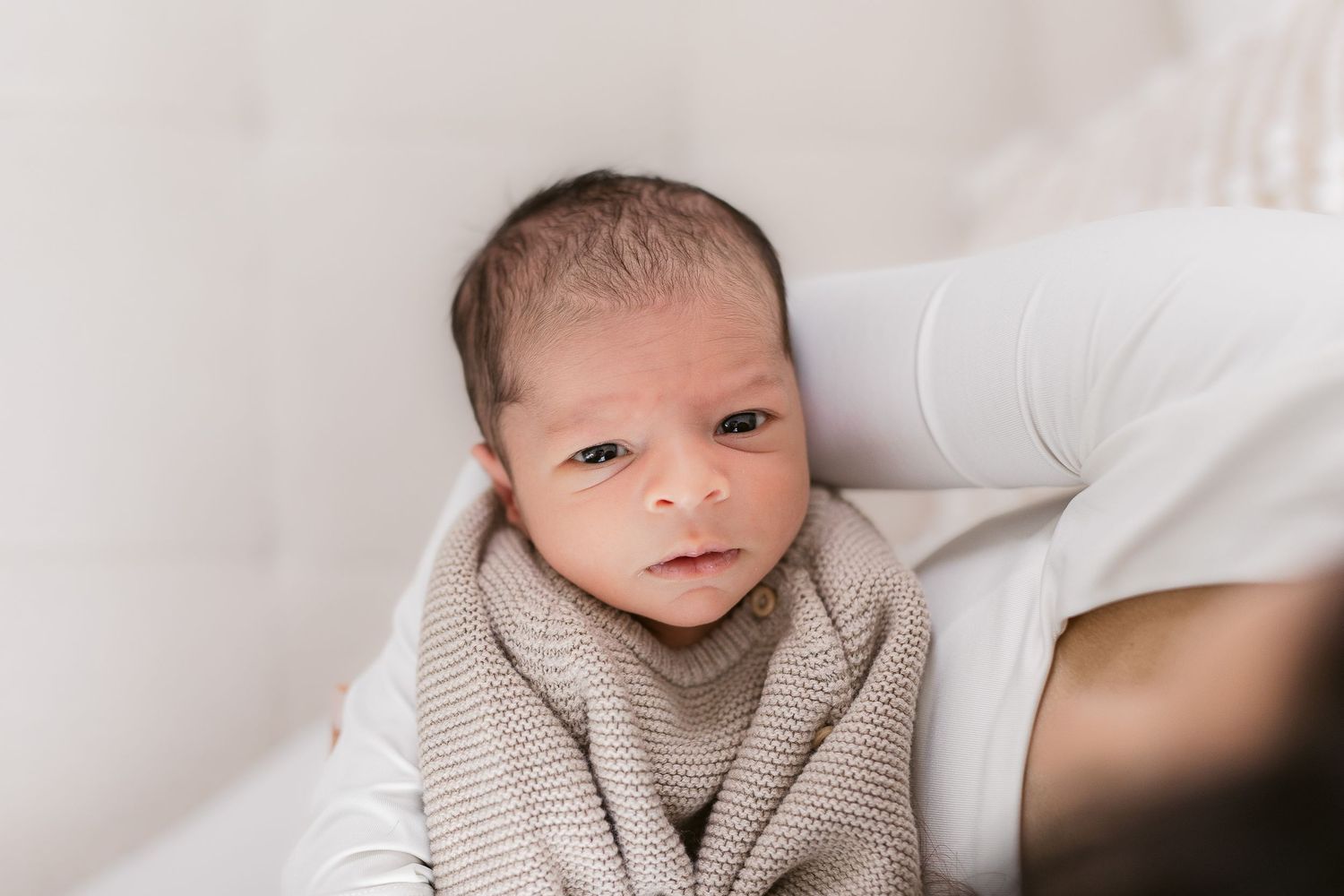 Newborn baby wrapped in beige knit blanket looks directly at camera.