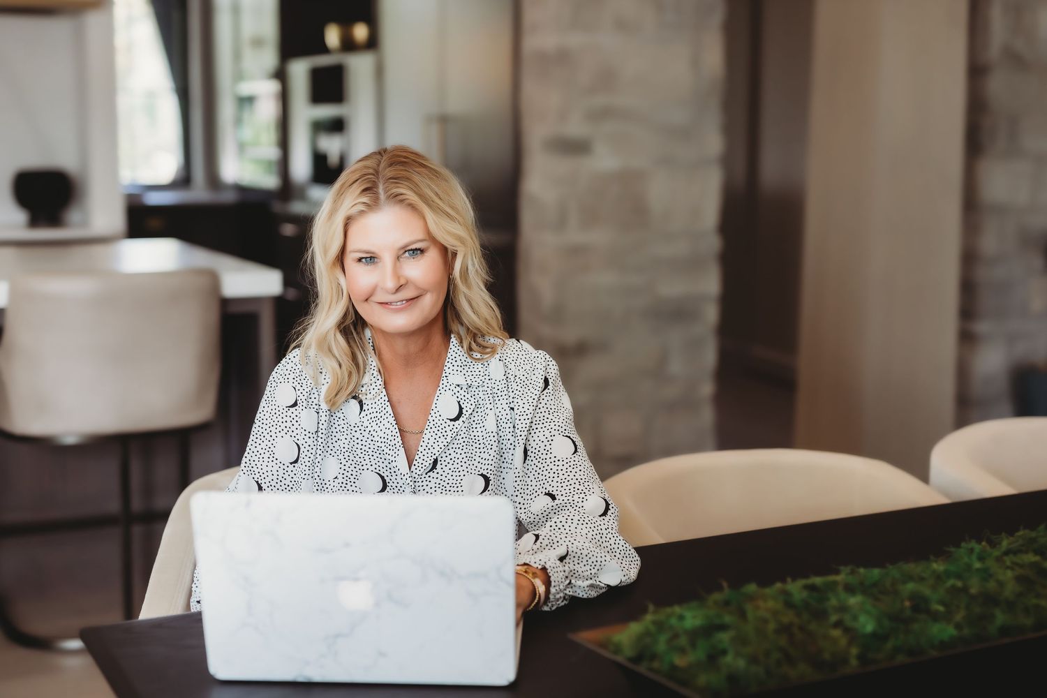 Professional lifestyle photo of someone in a black and white patterned dress sitting in a modern home office setting.