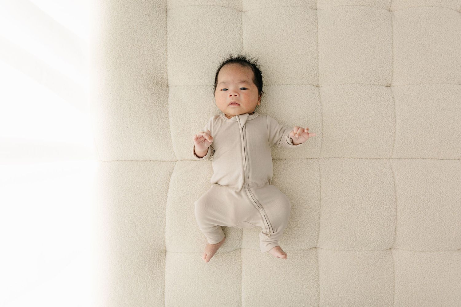Newborn baby in light clothing resting on white tufted surface.