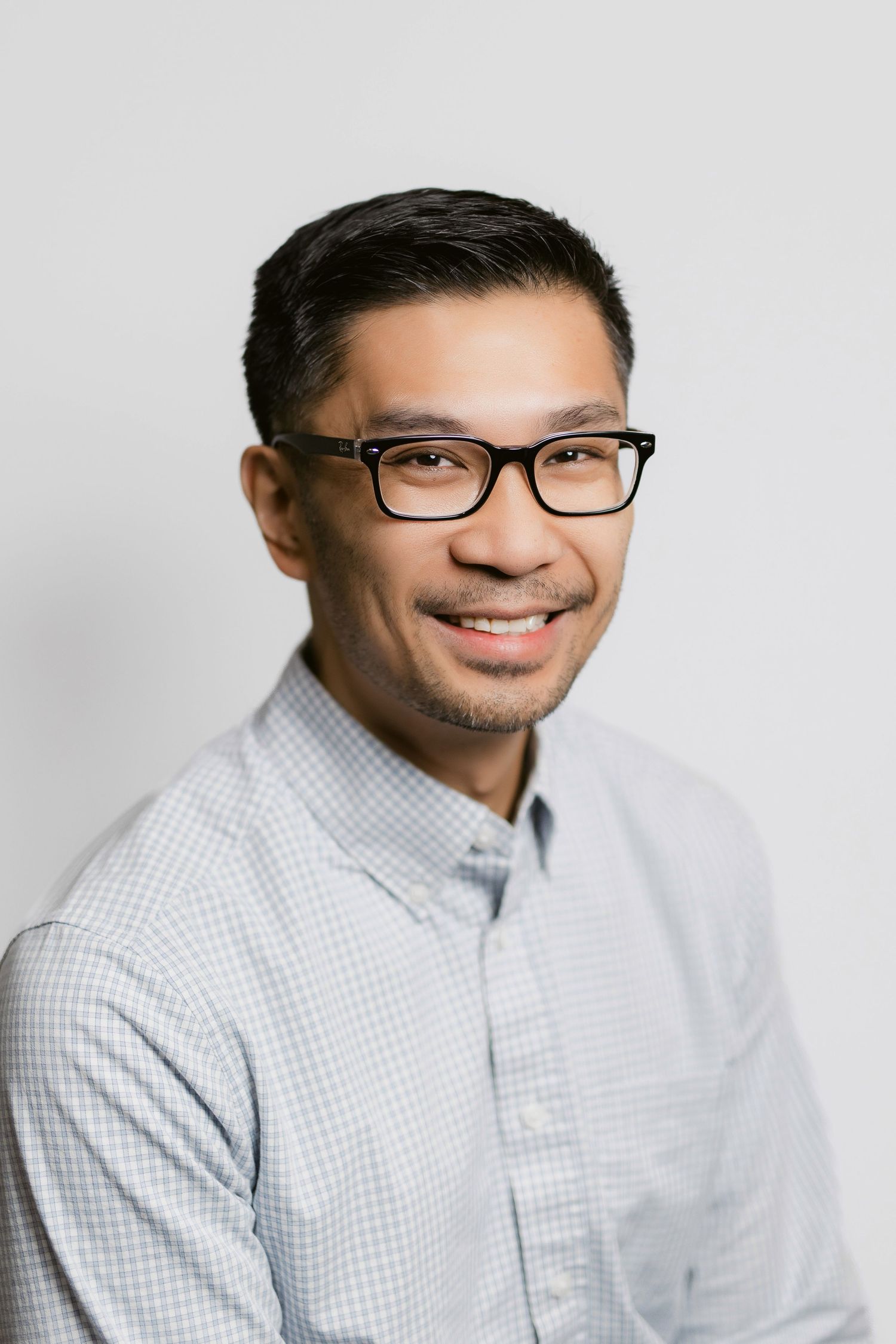 Professional headshots of person in glasses and checkered button-down shirt against light background.