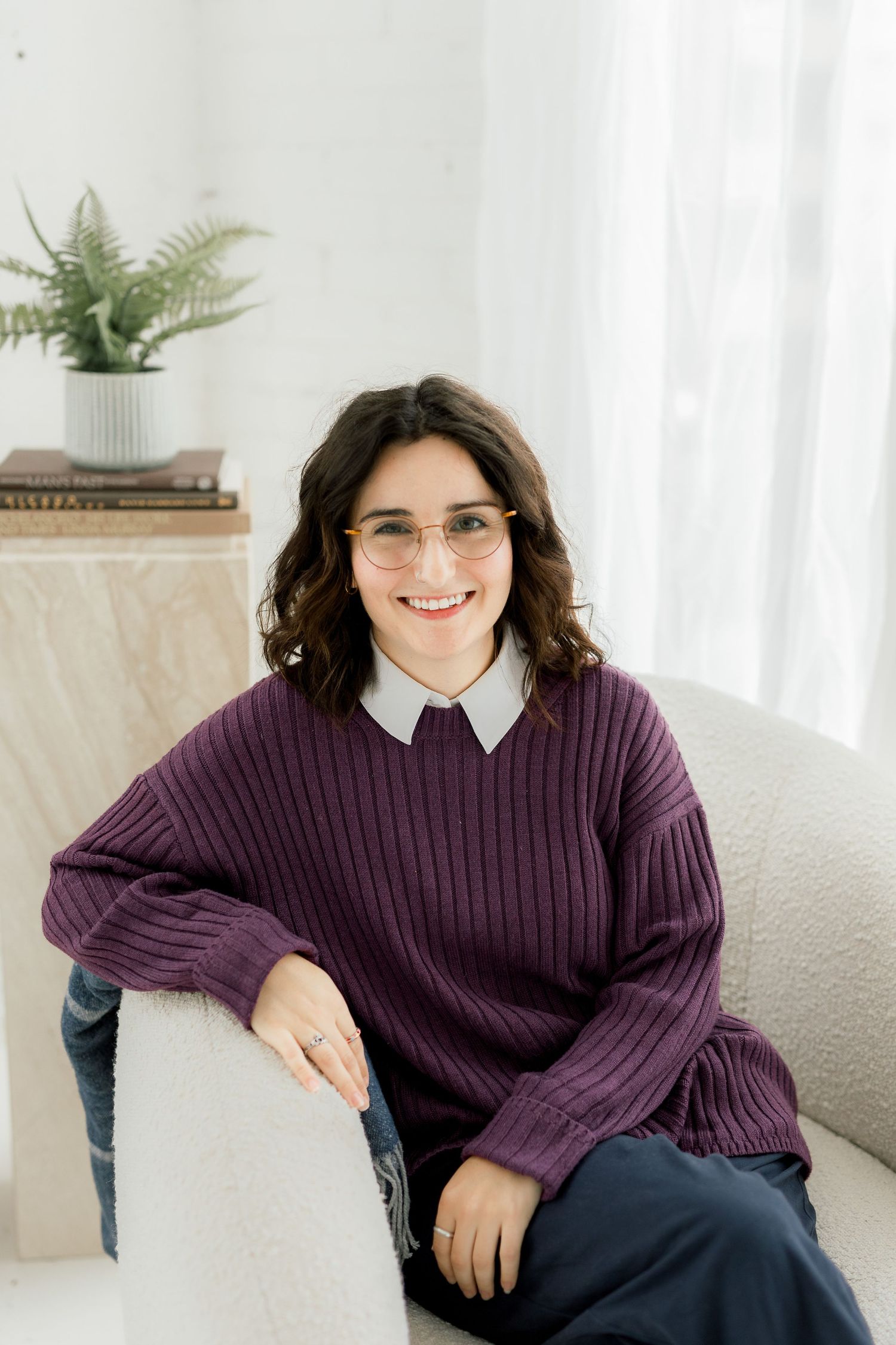 Person wearing purple sweater and white collar relaxes in bright studio environment.