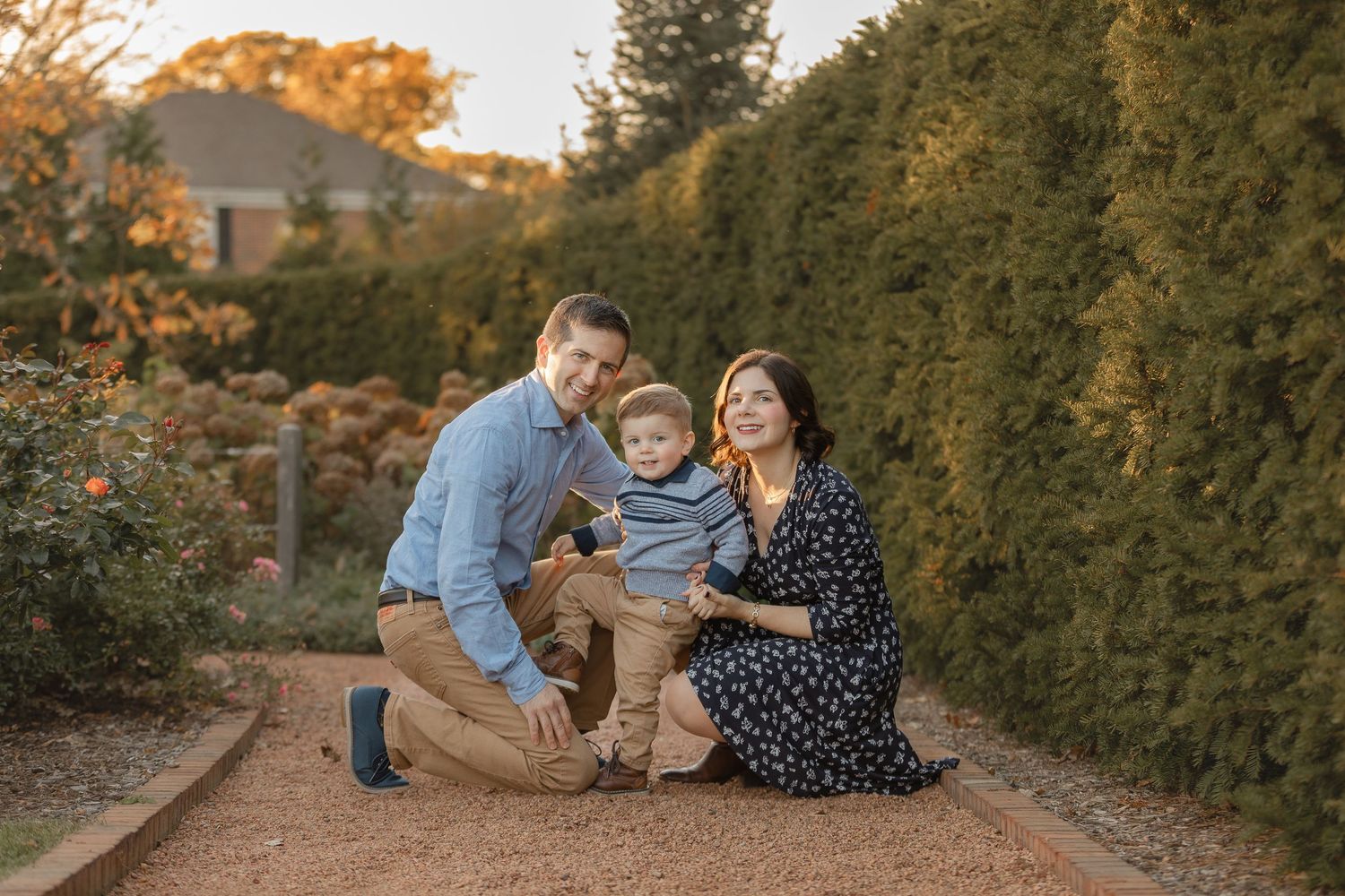 Family enjoying tender moments together on wooden path during autumn sunset photoshoot.