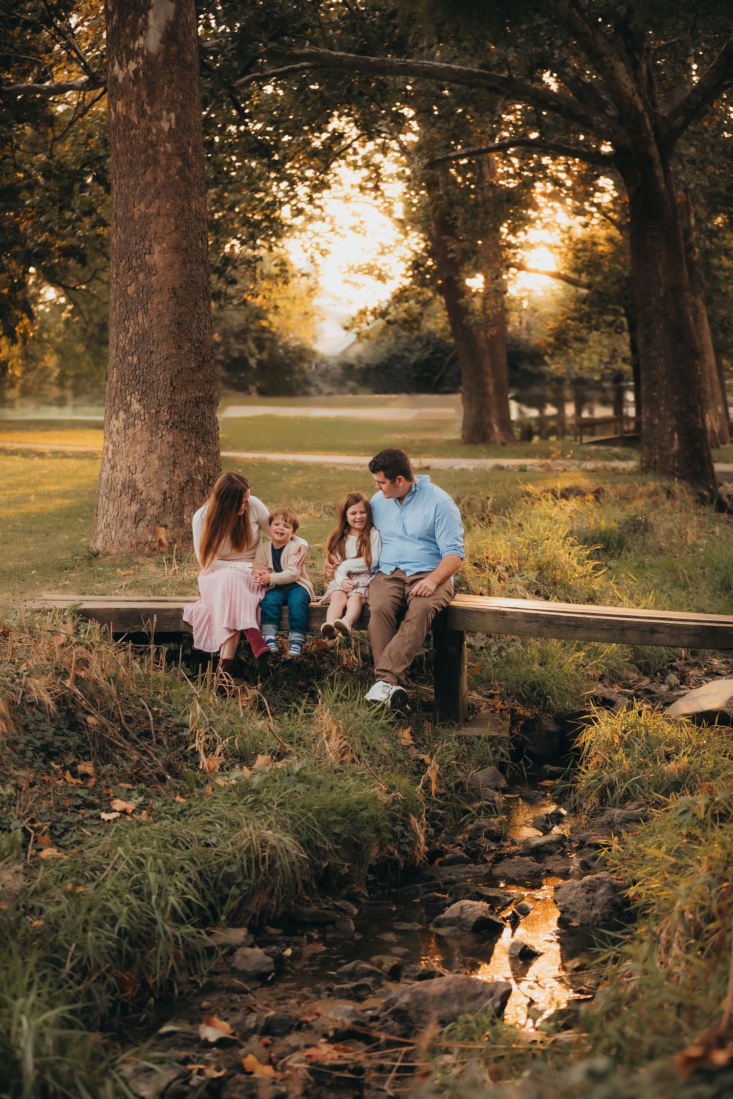 A warm family moment on a wooden bridge over a creek at sunset in a wooded park during autumn.
