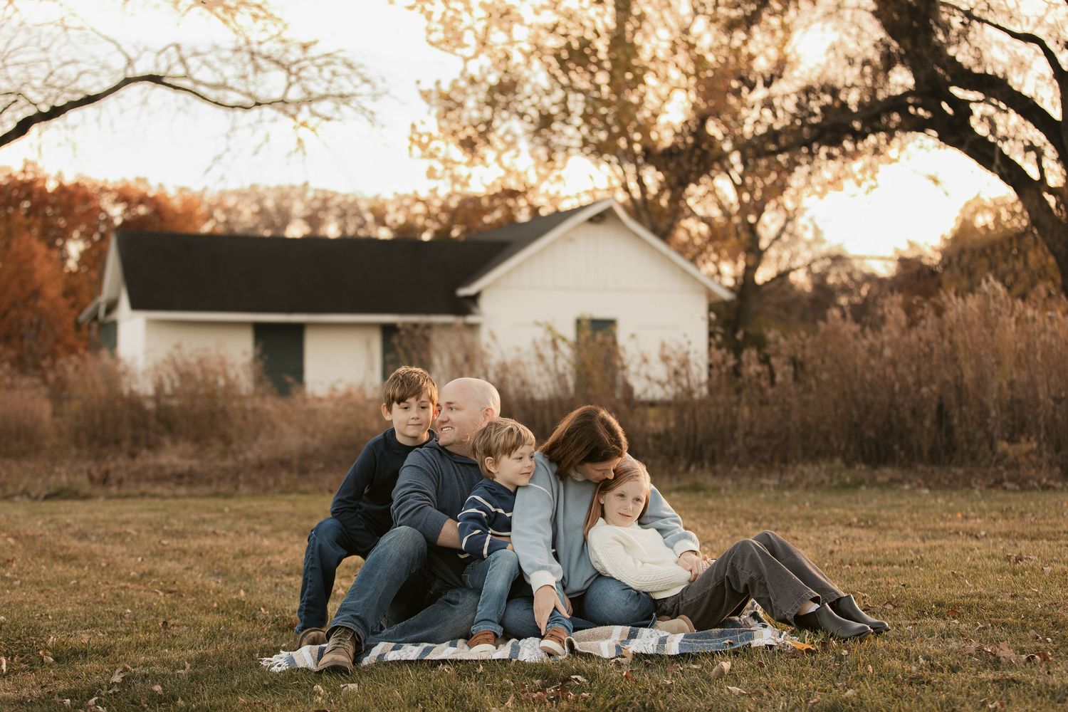 Family relaxing together on blanket during golden hour in rural field setting.