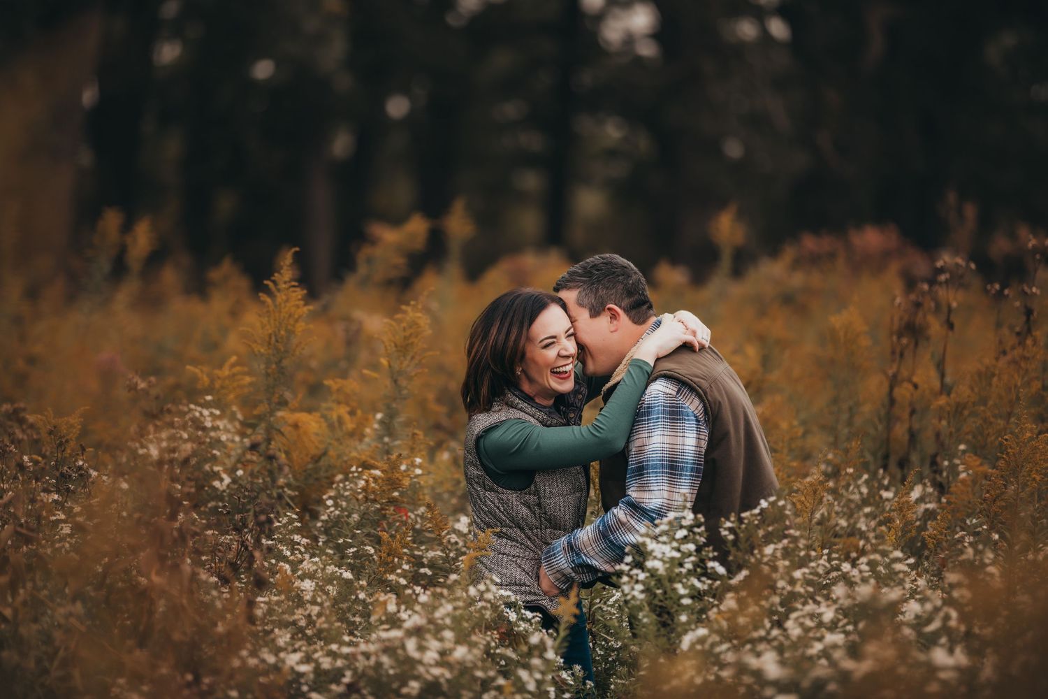 Couple embracing in field of autumn wildflowers at sunset.