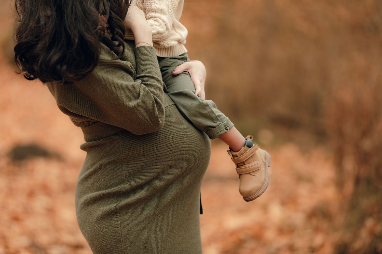 Autumn maternity photoshoot in forest with warm brown leaves and natural lighting.