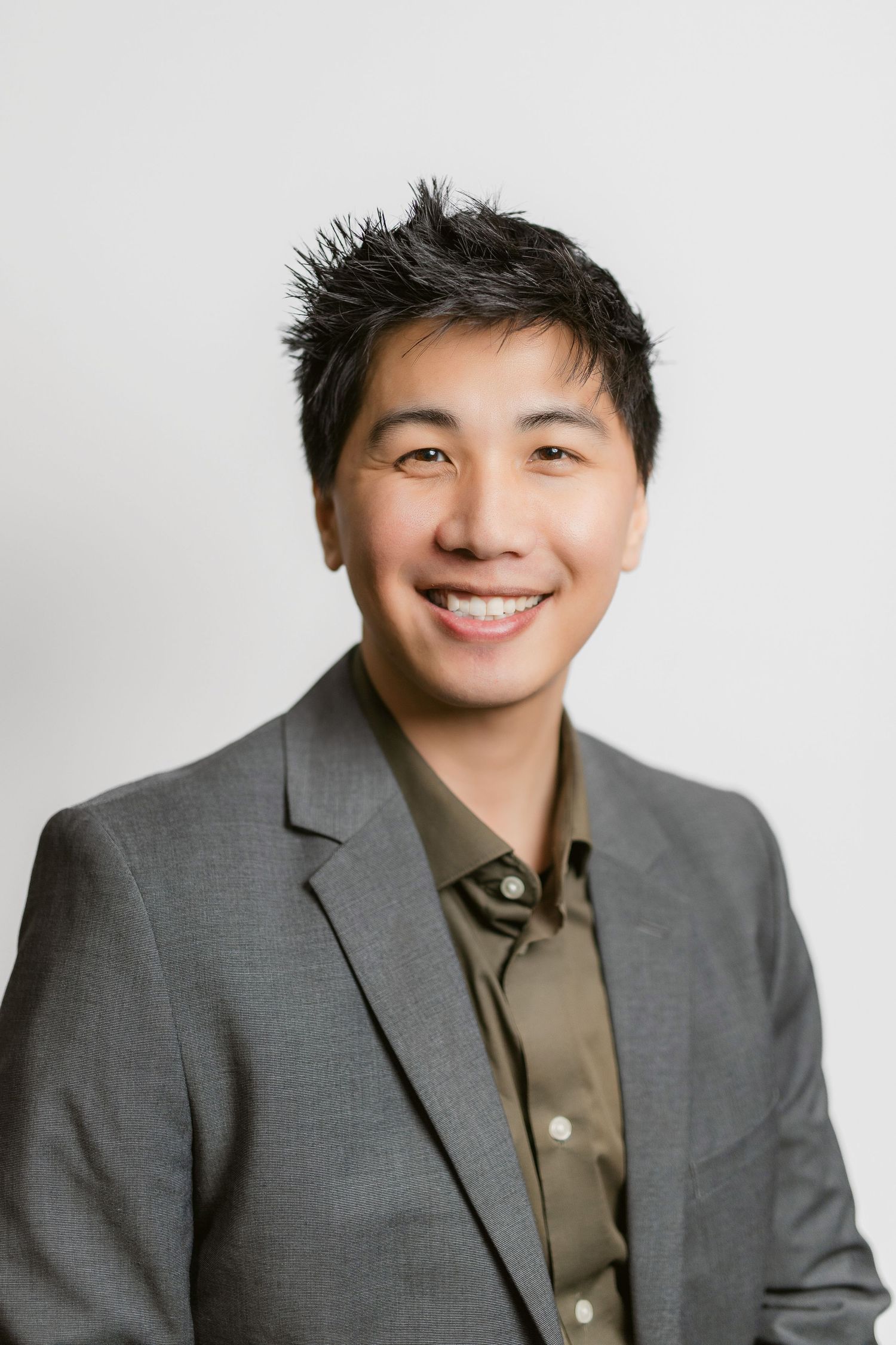 Professional headshots of a person in grey suit and olive shirt against white background.