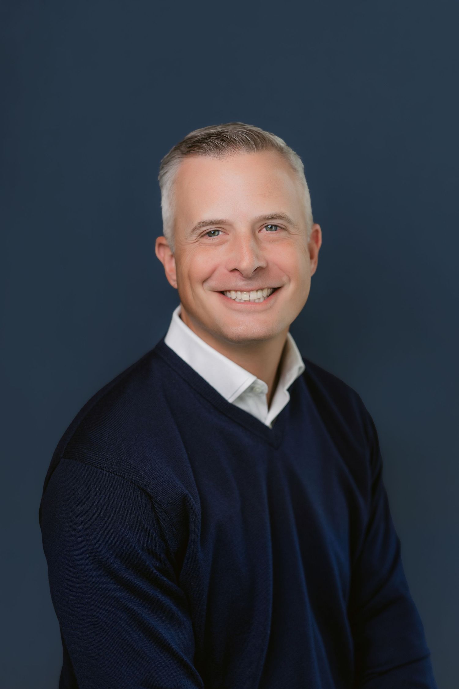 Professional headshots of person in navy sweater against dark blue background.