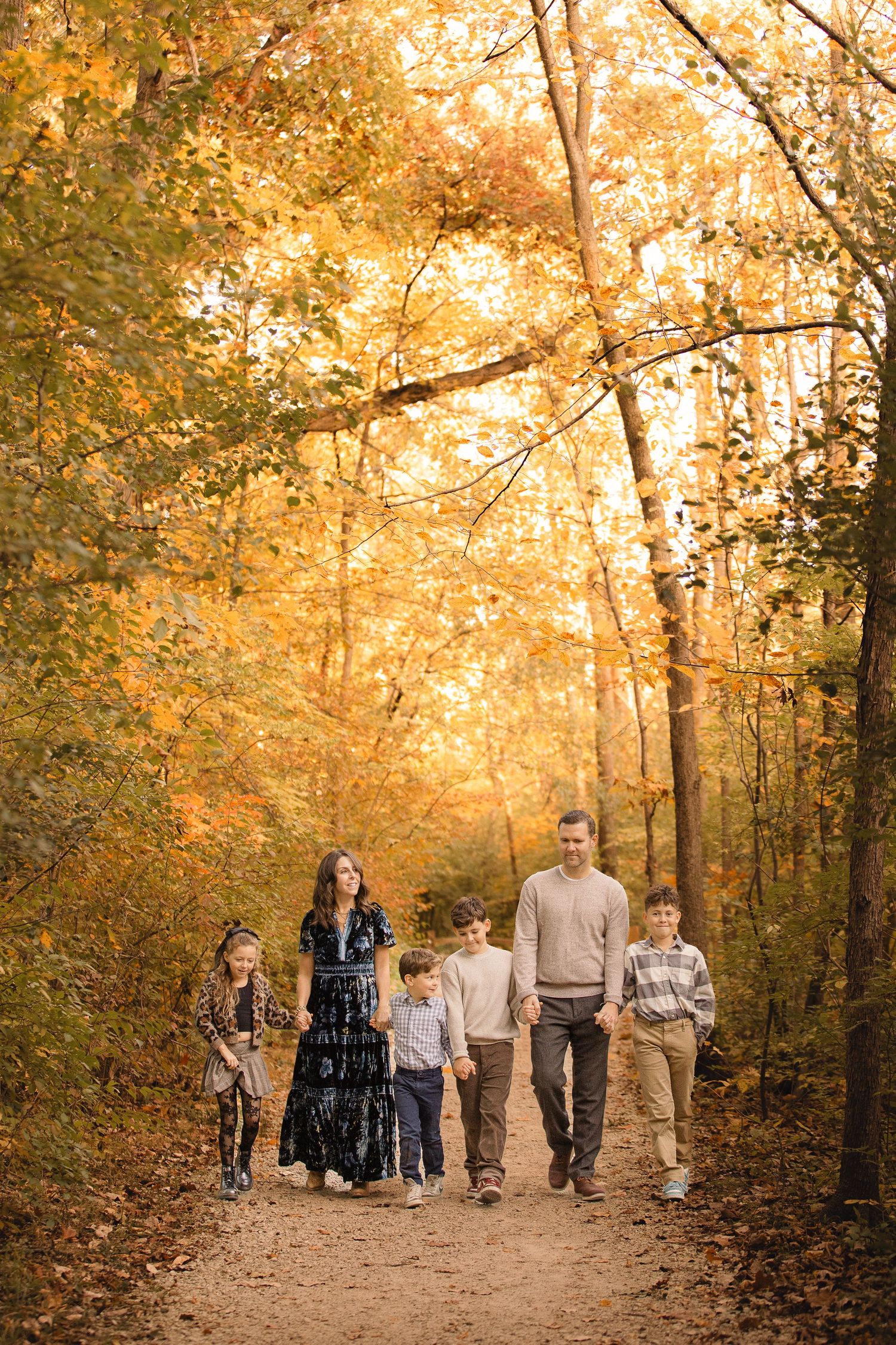 A group walks together on a wooded path surrounded by golden autumn foliage during sunset.