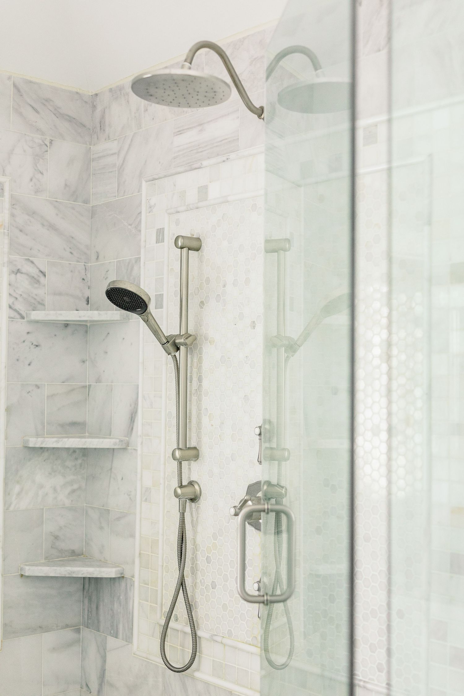Modern marble bathroom with glass shower enclosure featuring brushed nickel fixtures and built-in shelving.