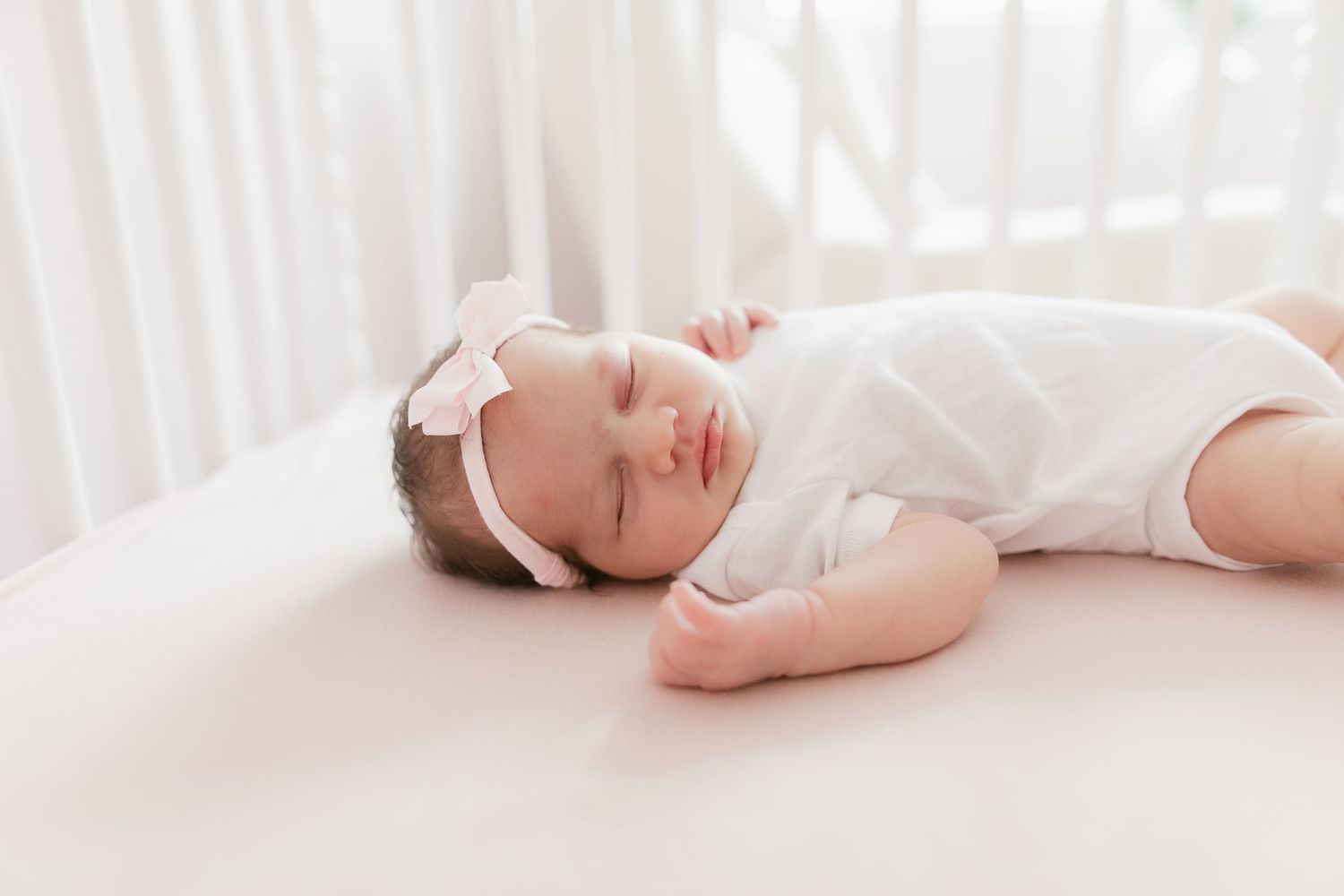 Infant wearing white clothing lying peacefully on white bedding.