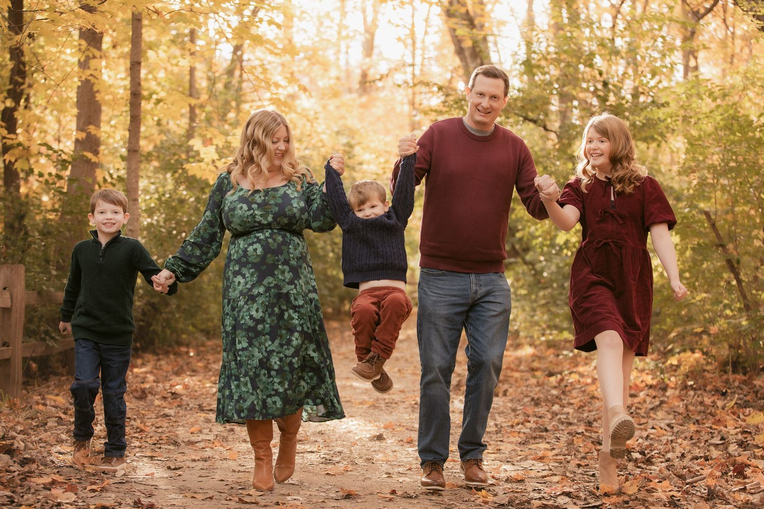 Group walking through autumn leaves on wooded path during fall photo session.