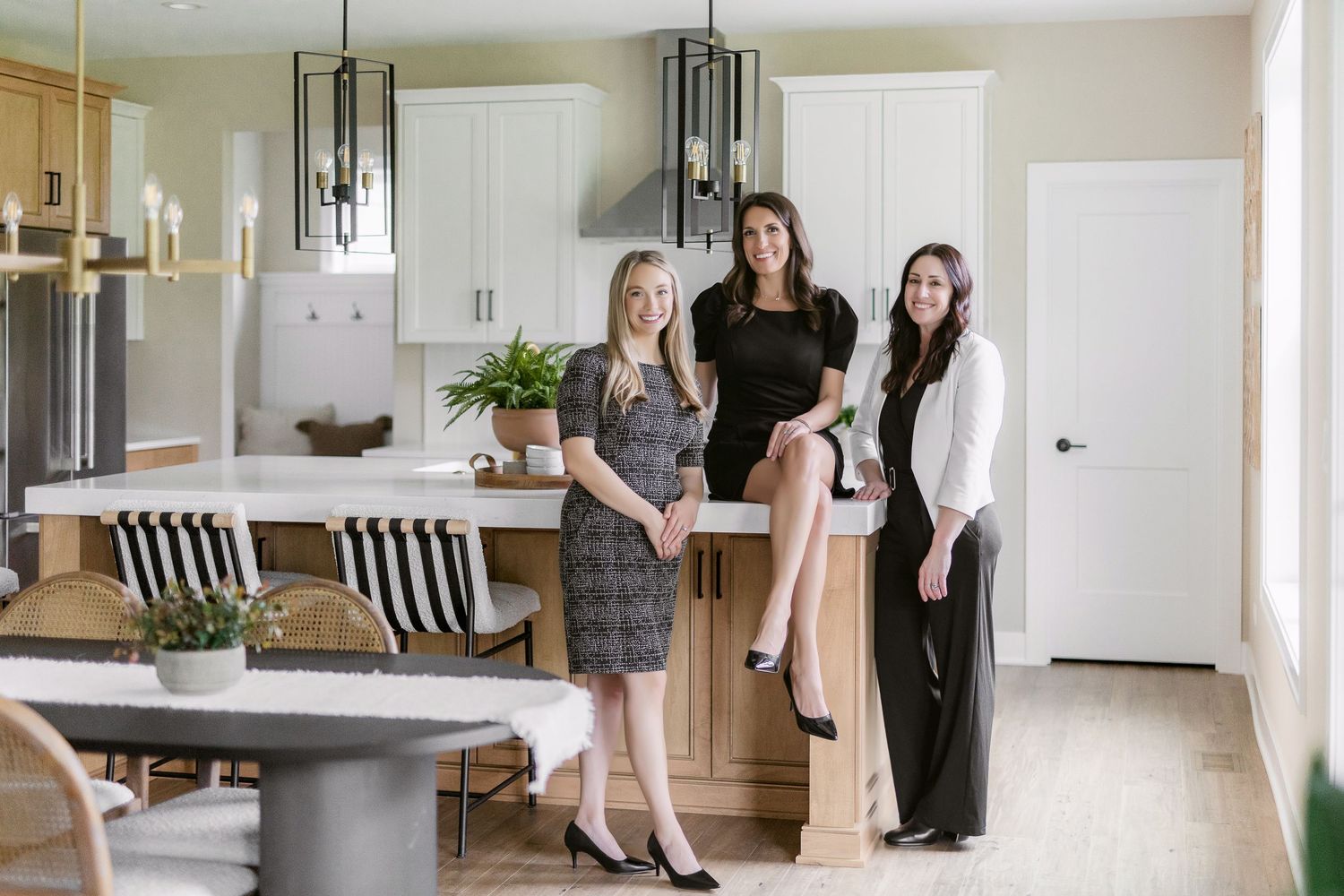 Three professionals pose together in modern white kitchen with black pendant lighting.