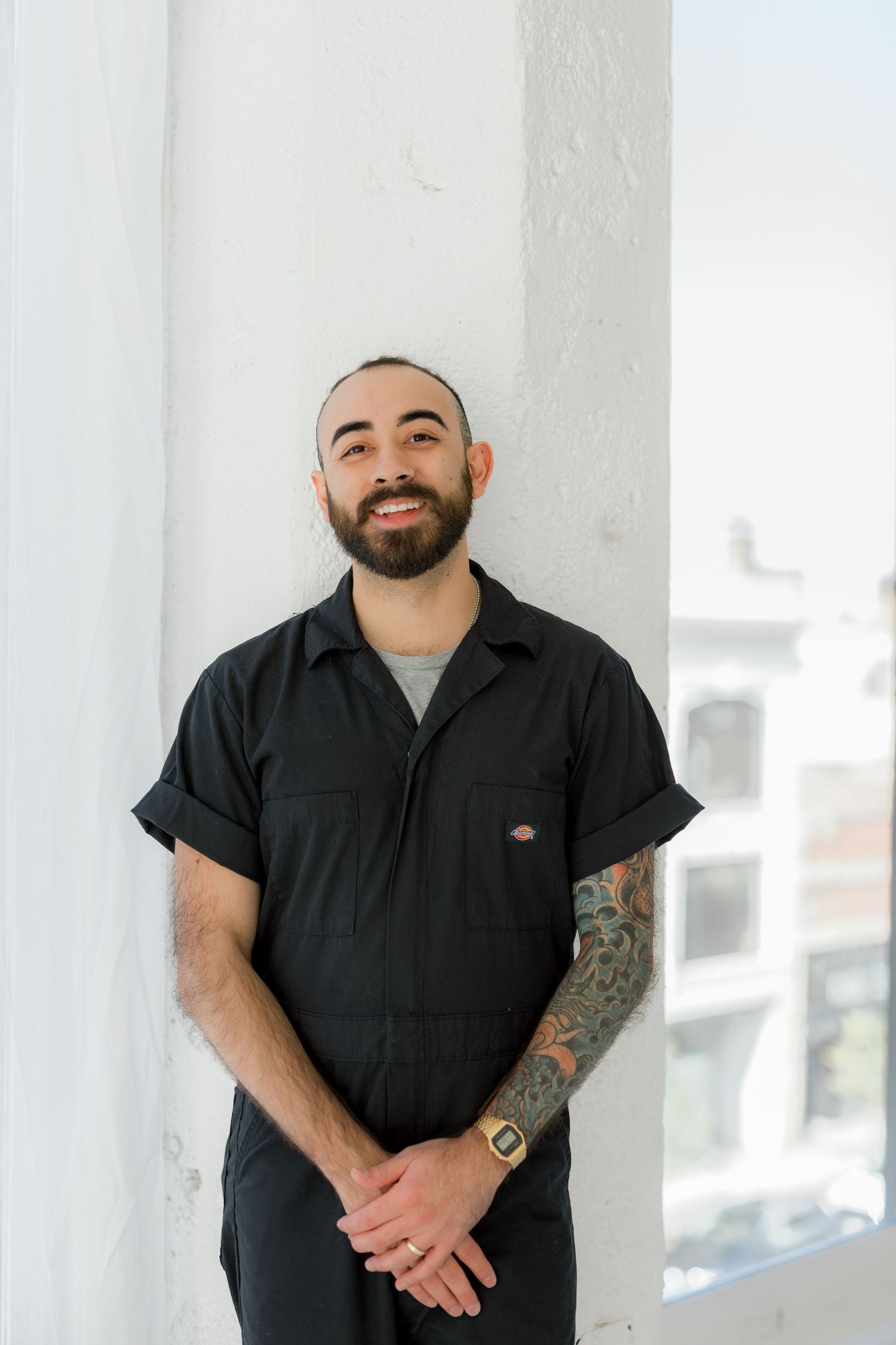 Portrait of someone in black work shirt with tattoo sleeve against white background.