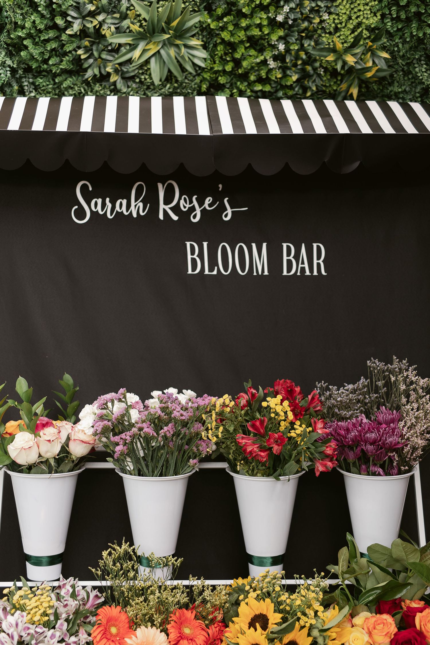 Sarah Rose's Bloom Bar floral display with colorful flowers in white cone holders under striped awning.