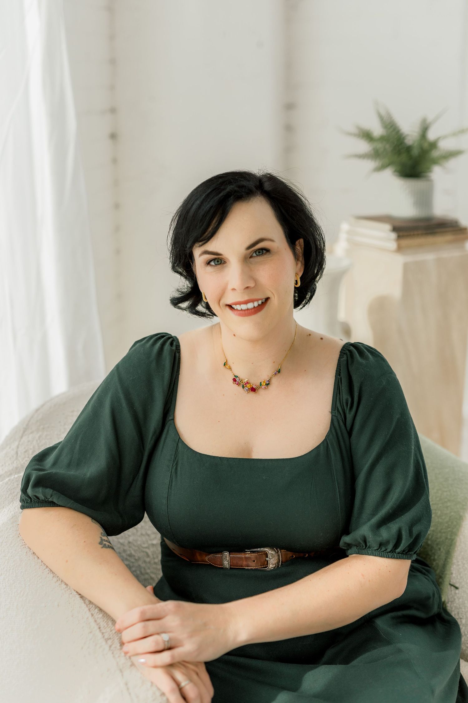 Professional portrait of someone wearing an elegant emerald green dress with puff sleeves and a brown belt.
