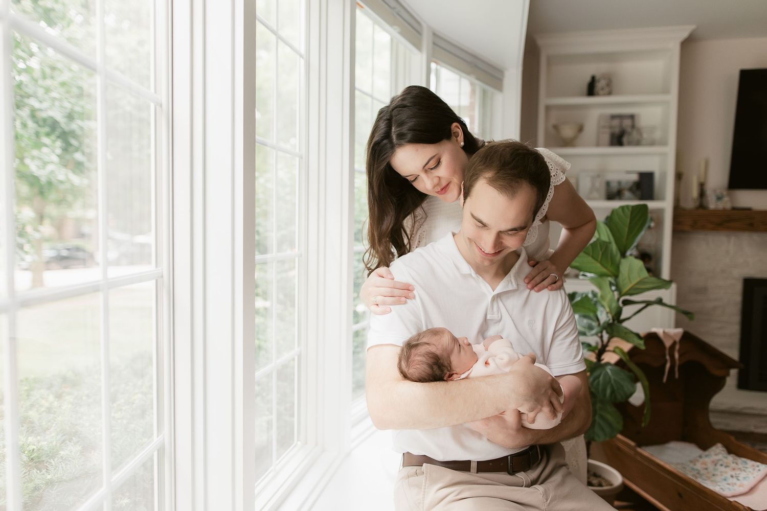 Tender moment by window with newborn baby in bright, airy setting.