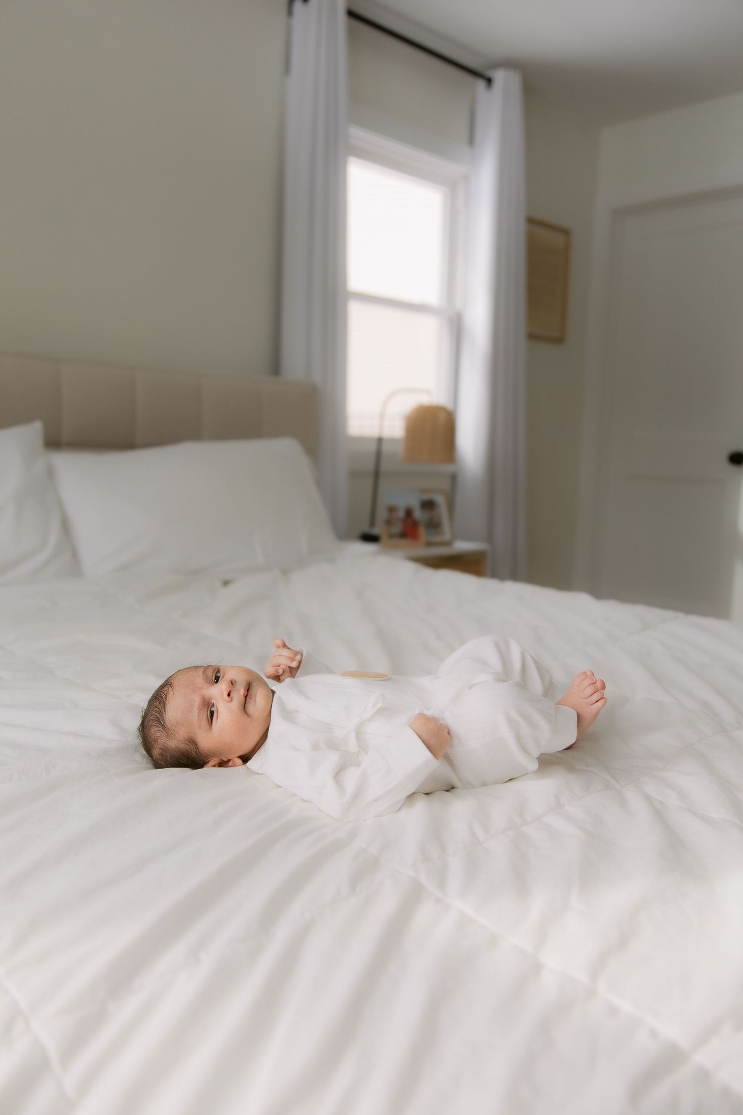 A baby lying peacefully on white bedding in a sunlit room with clean minimal decor.